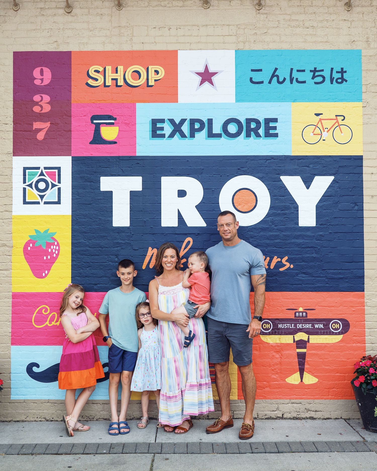 A family stands together against a vibrant mural wall featuring shop and explore themes.