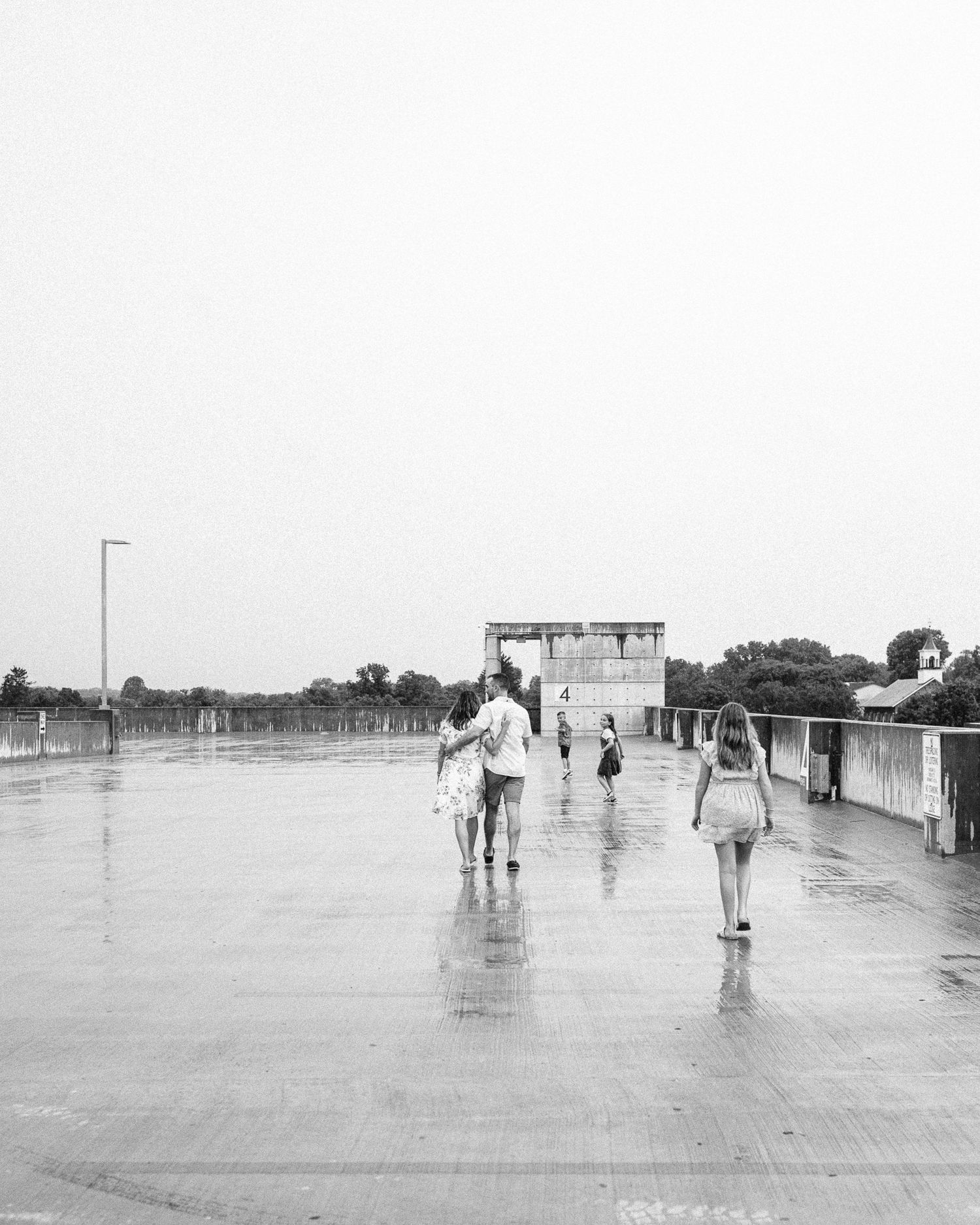A black and white photo of people walking on a wet surface with a structure in the background.