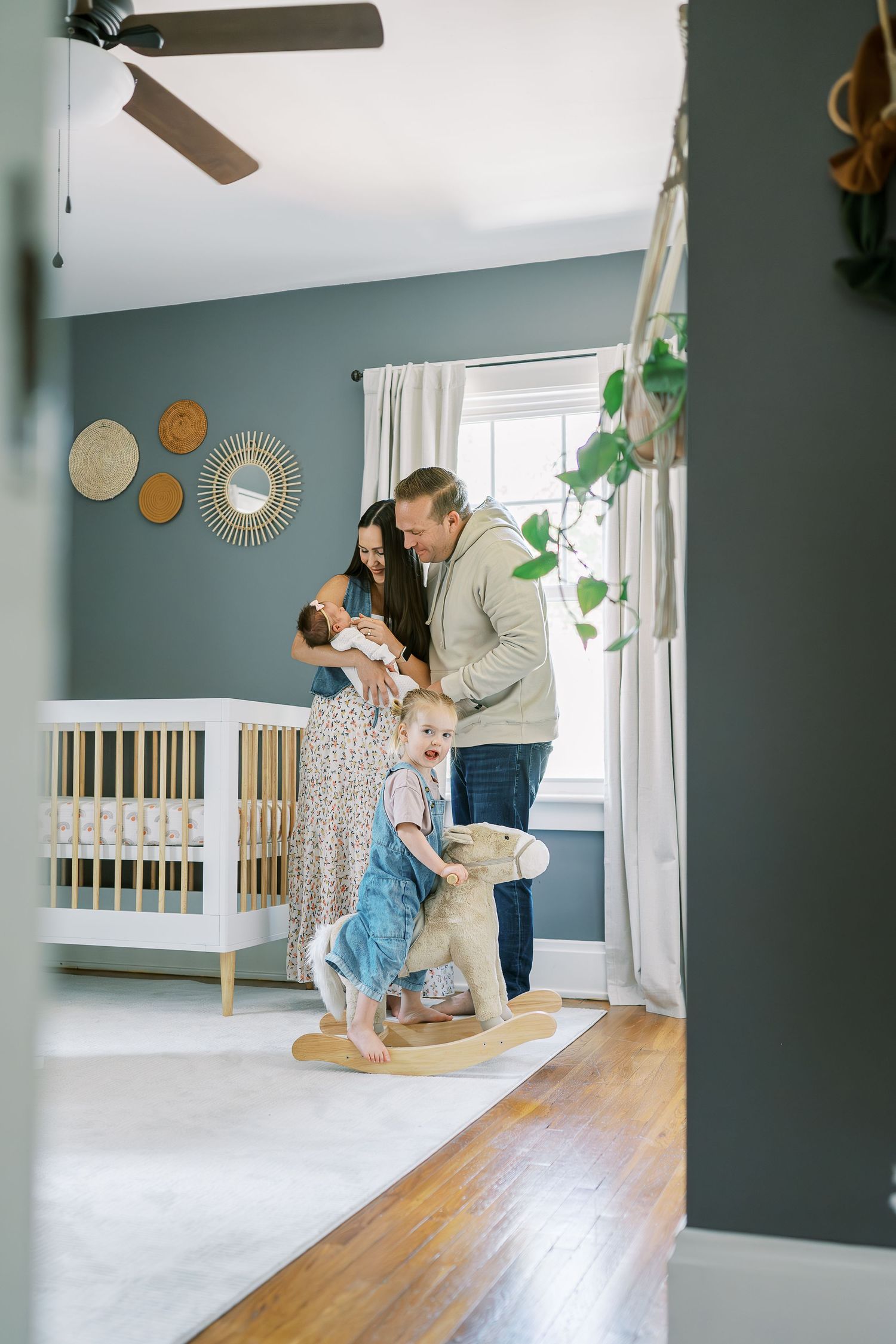 A nursery room with blue-gray walls features a wooden crib, decorative wall art, and a rocking horse.