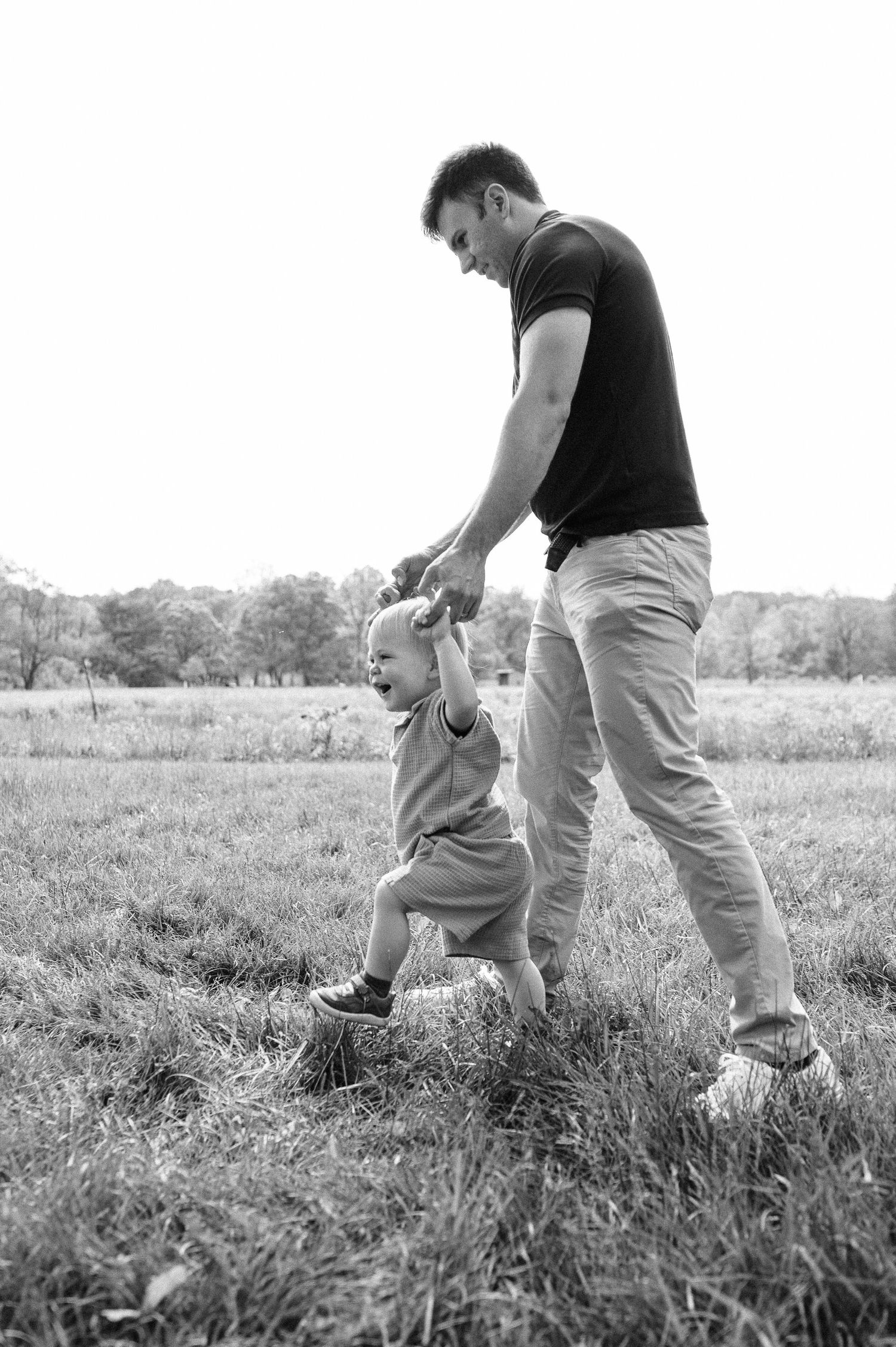 A black and white photo of parent and child walking together in a grassy field.