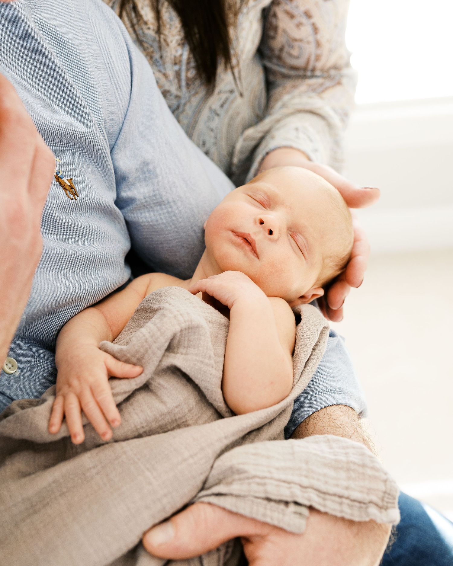 A peaceful sleeping newborn baby wearing gray clothing rests in someone's arms wearing a blue polo shirt.