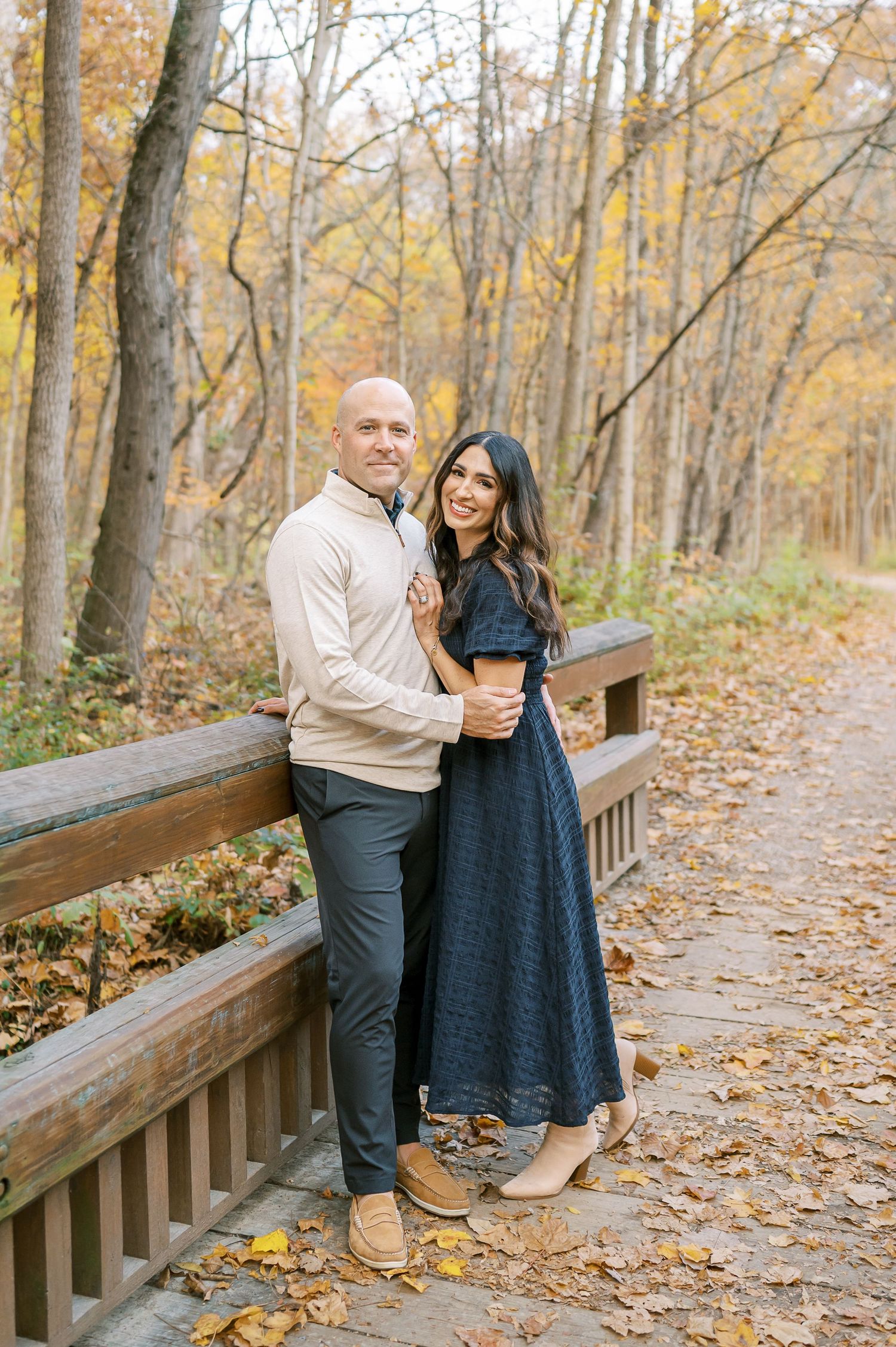Couple shares intimate moment on wooden walkway surrounded by fall foliage.