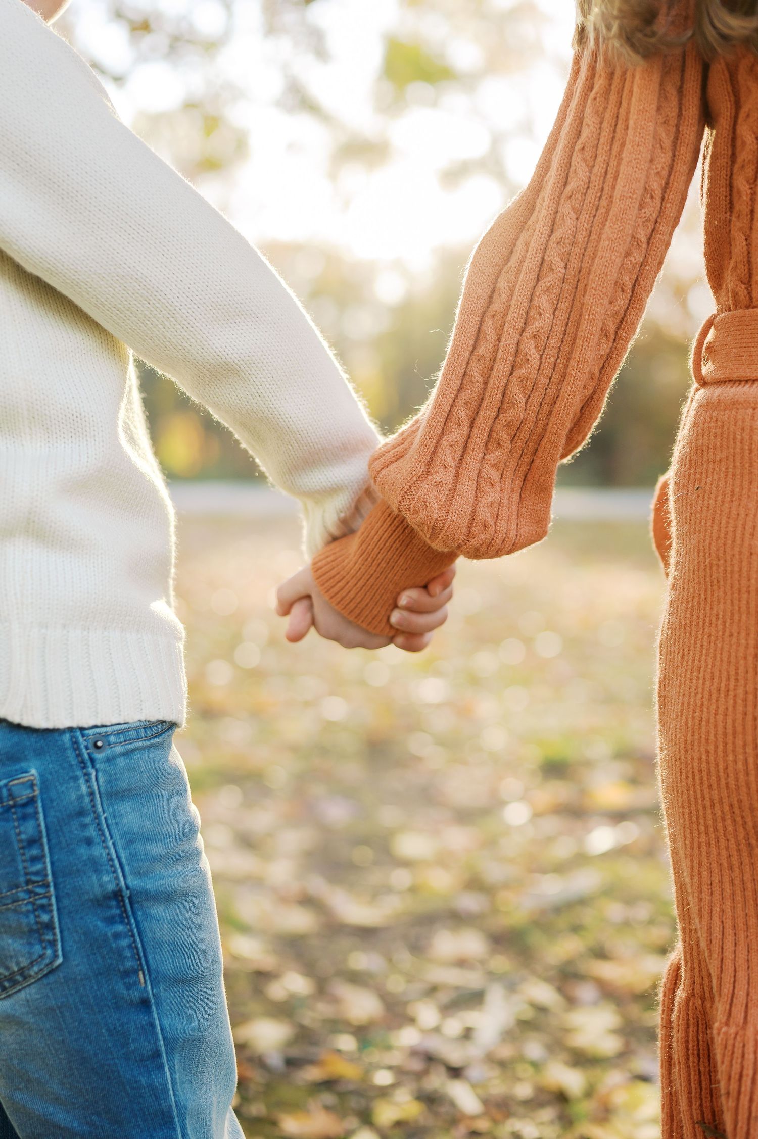 Detail shot of blue jeans and orange knit sweater textures in warm autumn lighting.