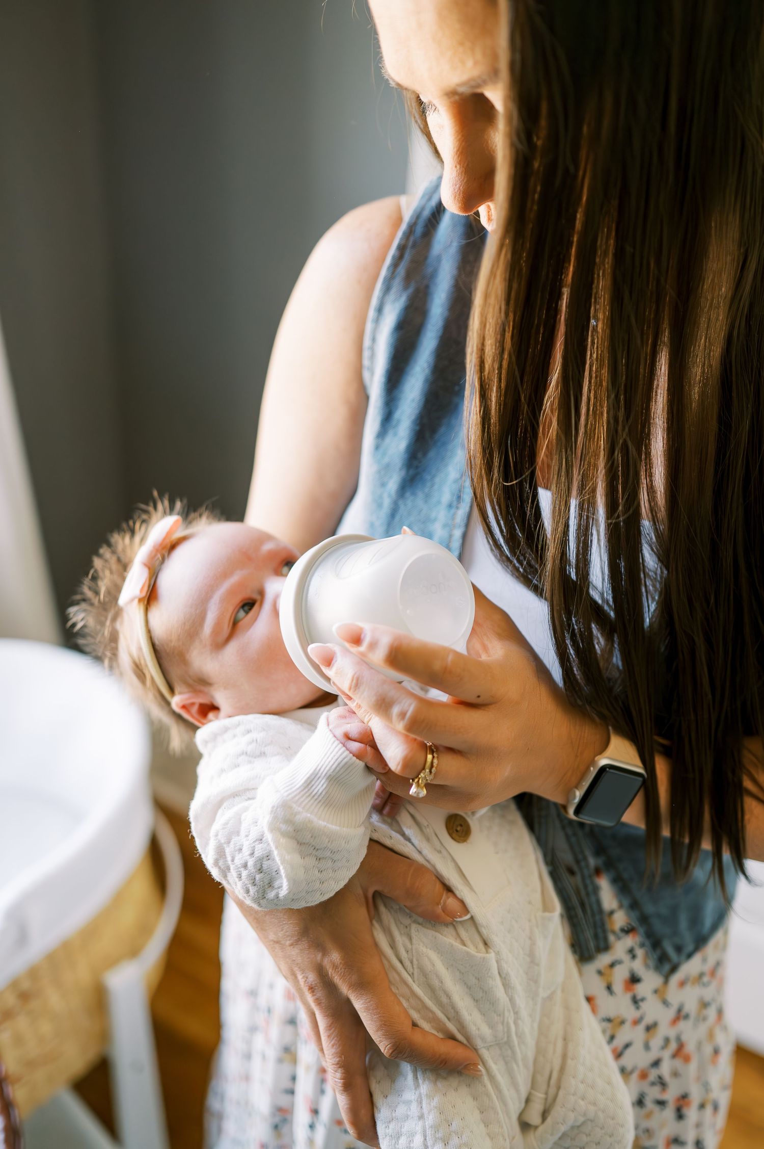 Person in floral dress holding and feeding small infant.