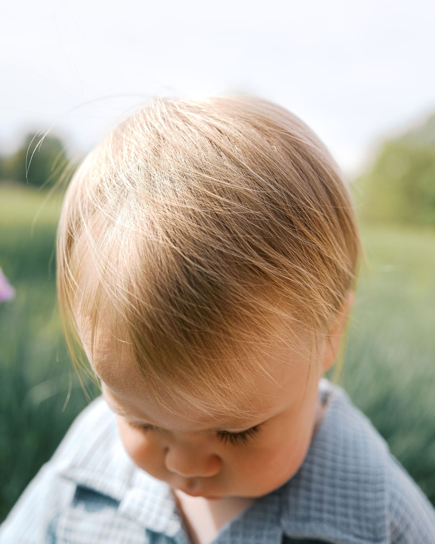 Toddler in checkered shirt looking down thoughtfully in outdoor nature setting.