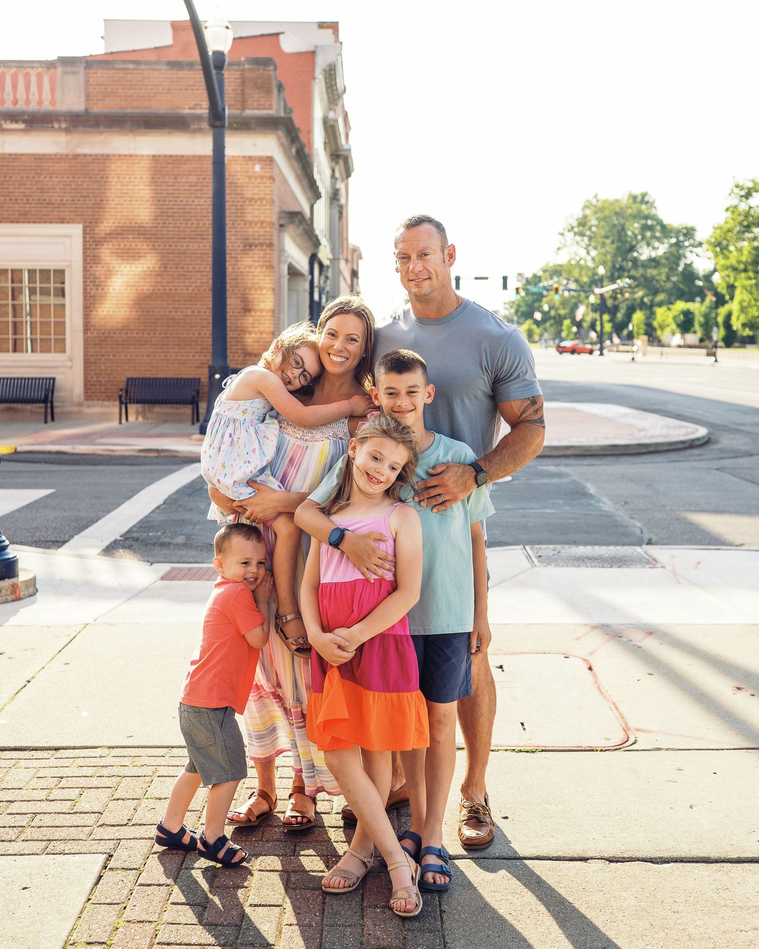 Family group poses together on brick sidewalk during sunny afternoon.