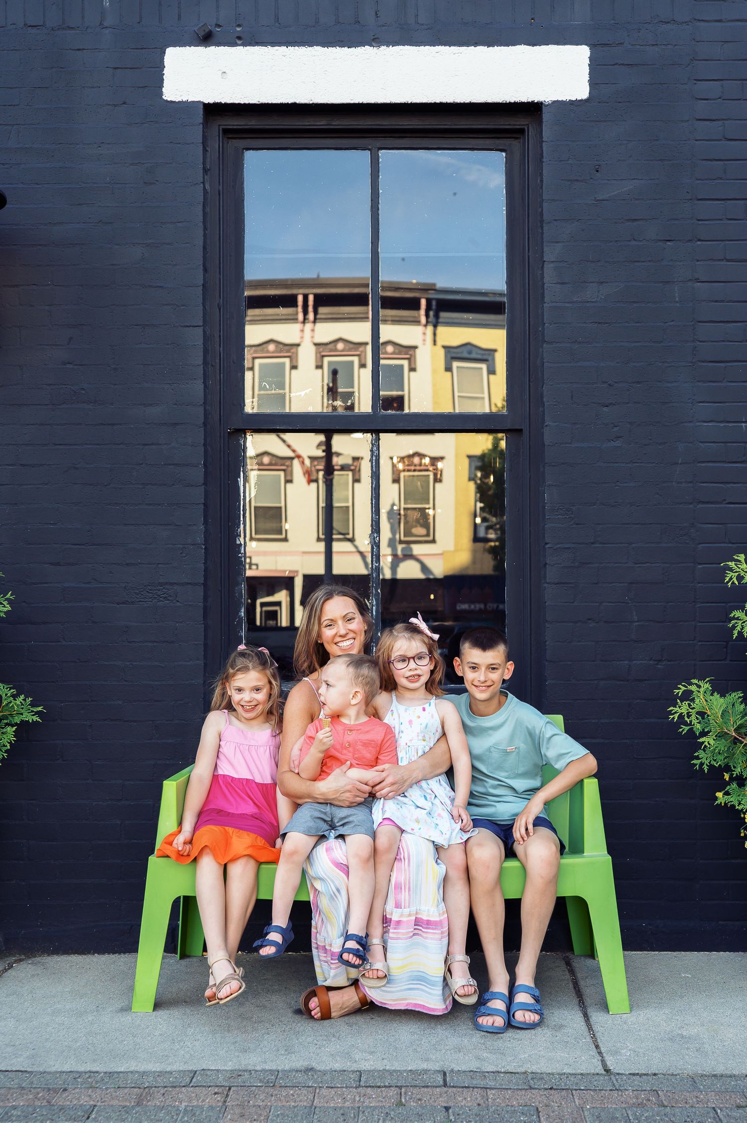 Family sitting together on green chairs against dark painted wall with reflective window.
