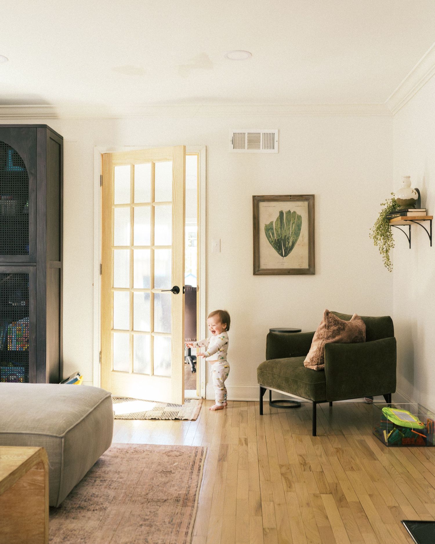 A sunlit living room with hardwood floors, french doors, and botanical wall art.