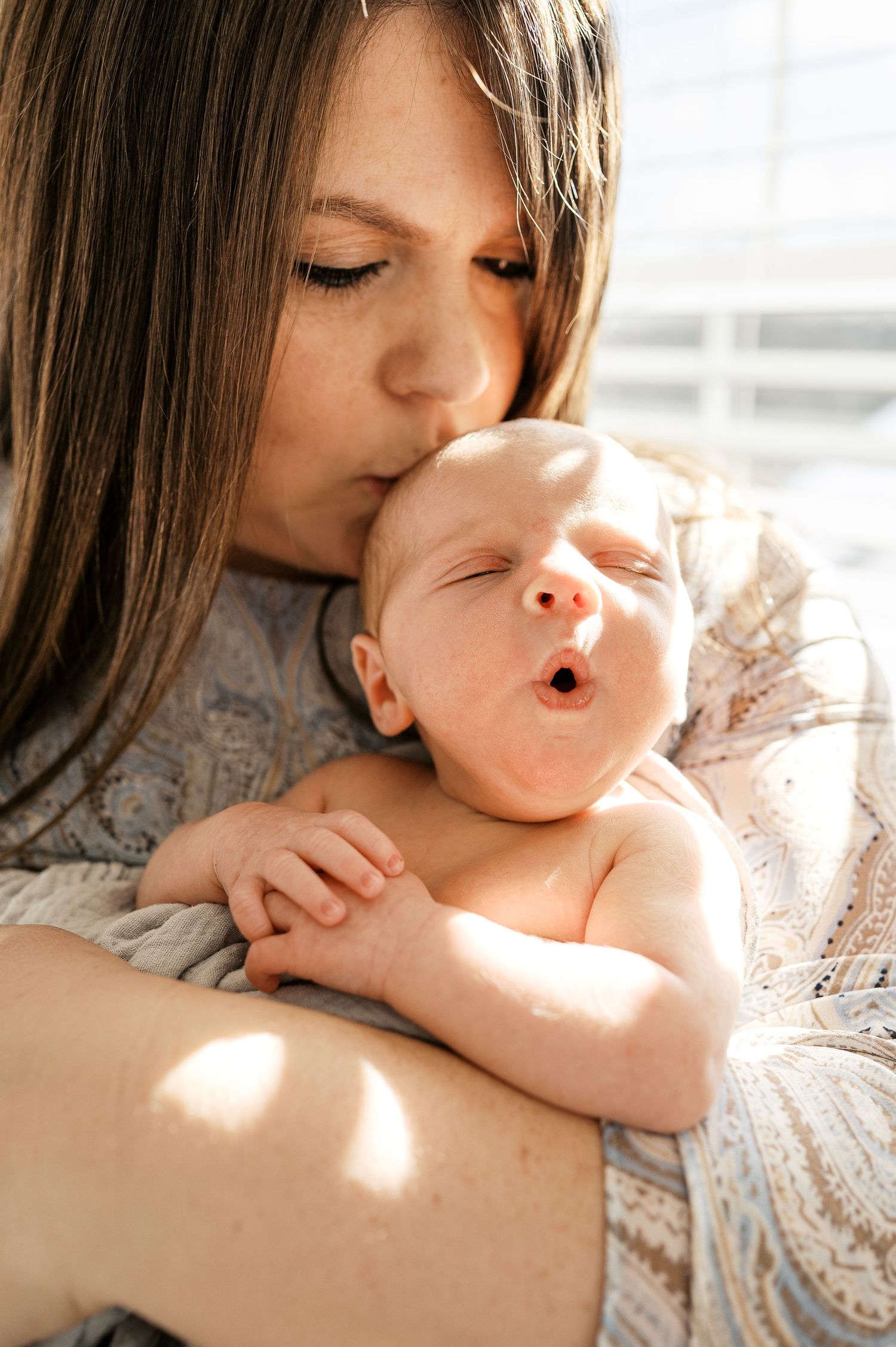 Tender moment between parent and newborn baby in soft natural window light.