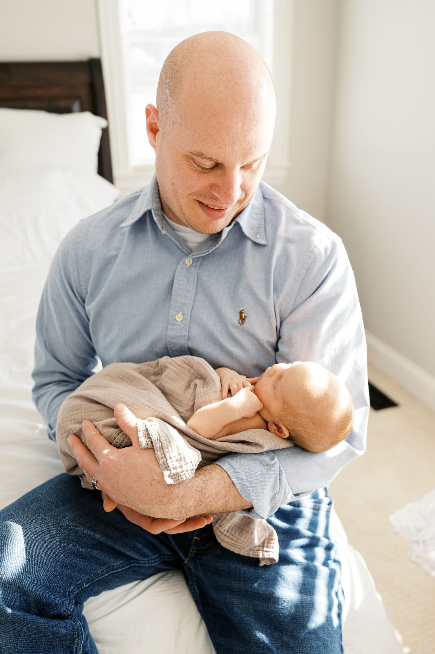 A tender moment between parent and newborn baby in a sunlit bedroom.