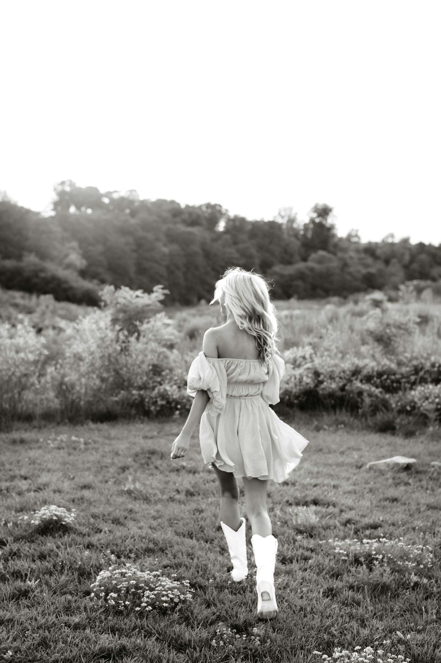 Girl in a white dress twirling in a meadow at golden hour, shot in black and white.