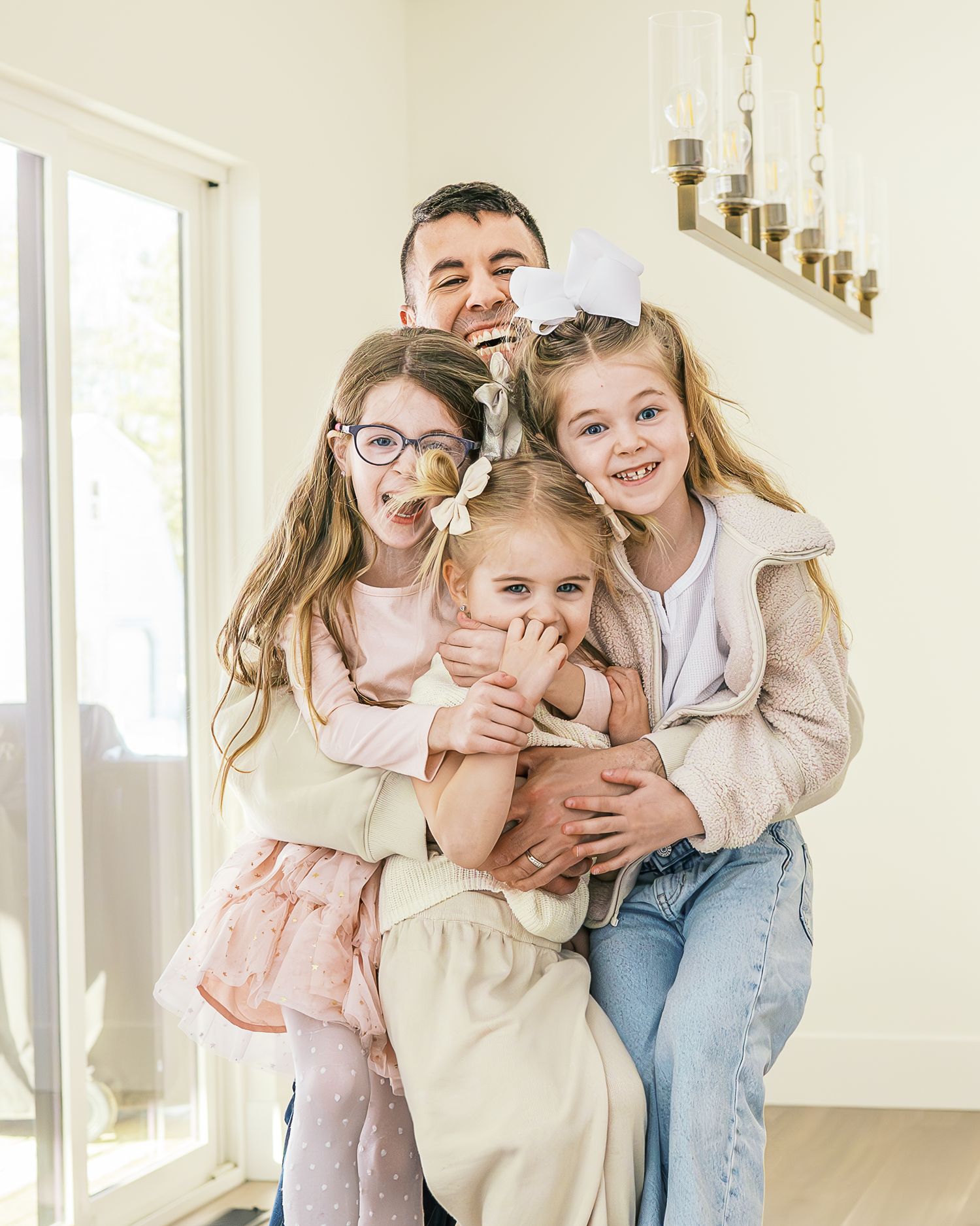 Family plays and cuddles together in bright sunlit room wearing coordinated pink and cream outfits.