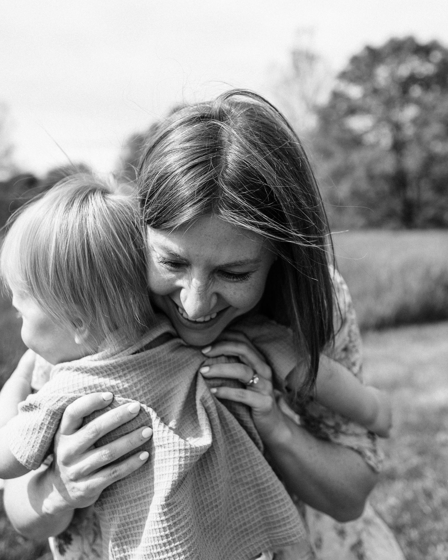 An intimate black and white portrait of a tender family embrace outdoors.