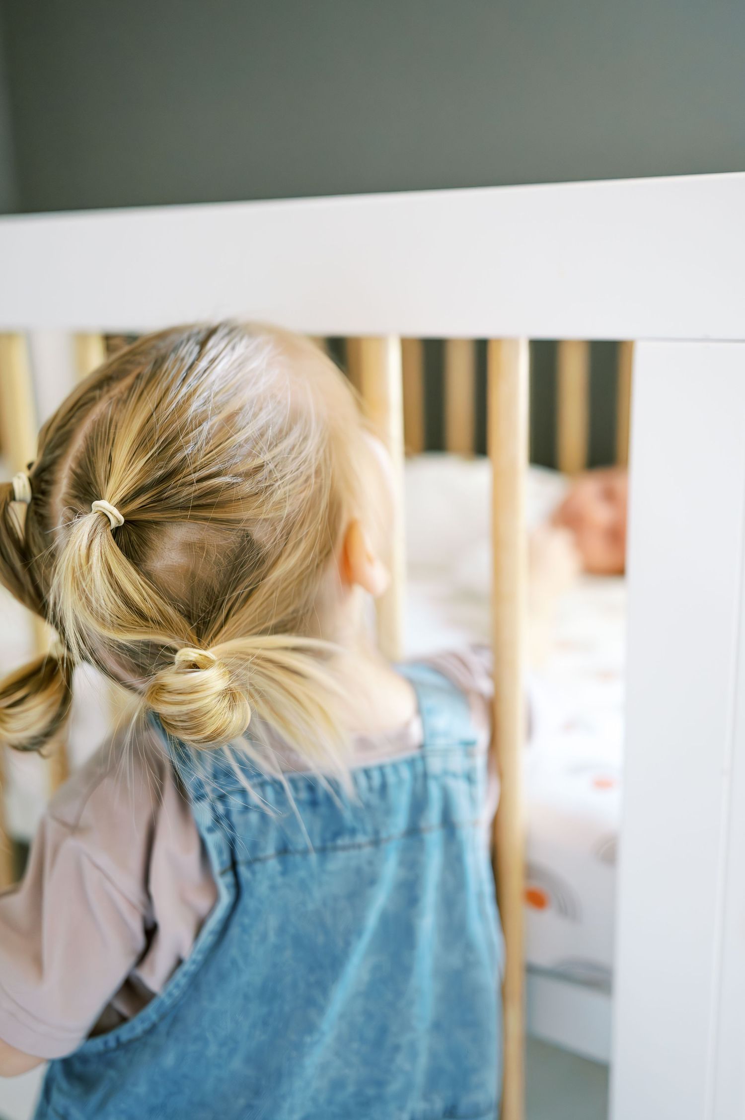Back view of person in denim overalls looking through crib slats.