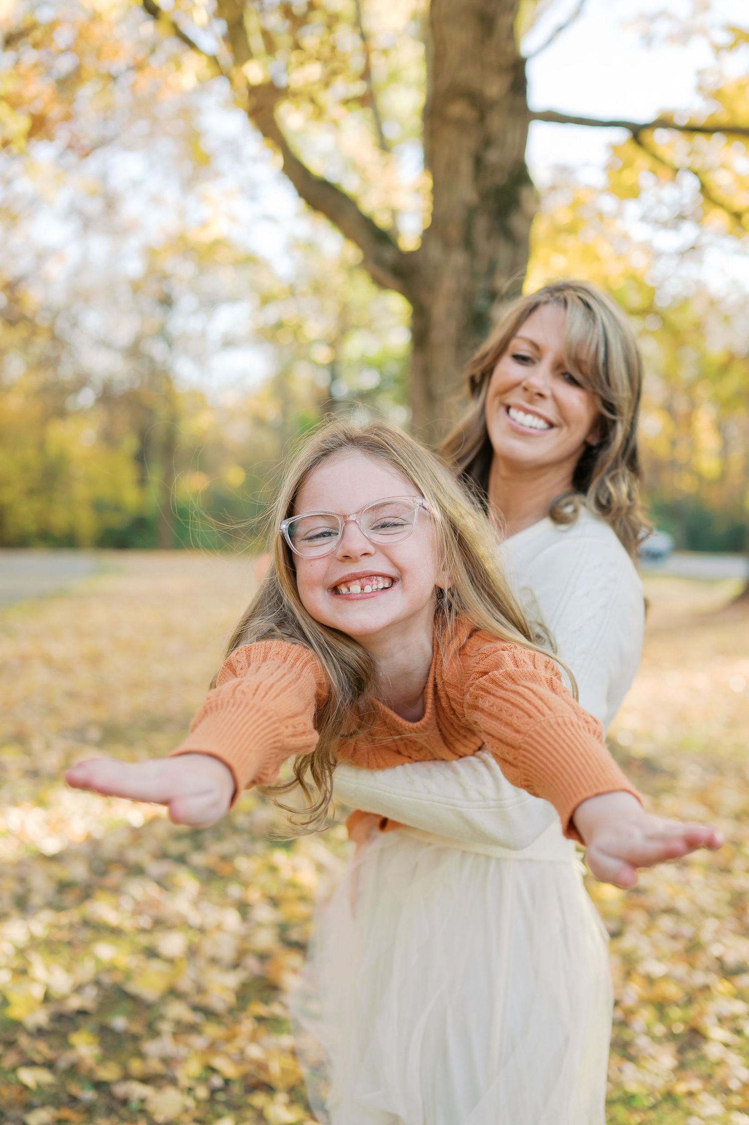 Person in orange sweater spinning joyfully among fallen autumn leaves.