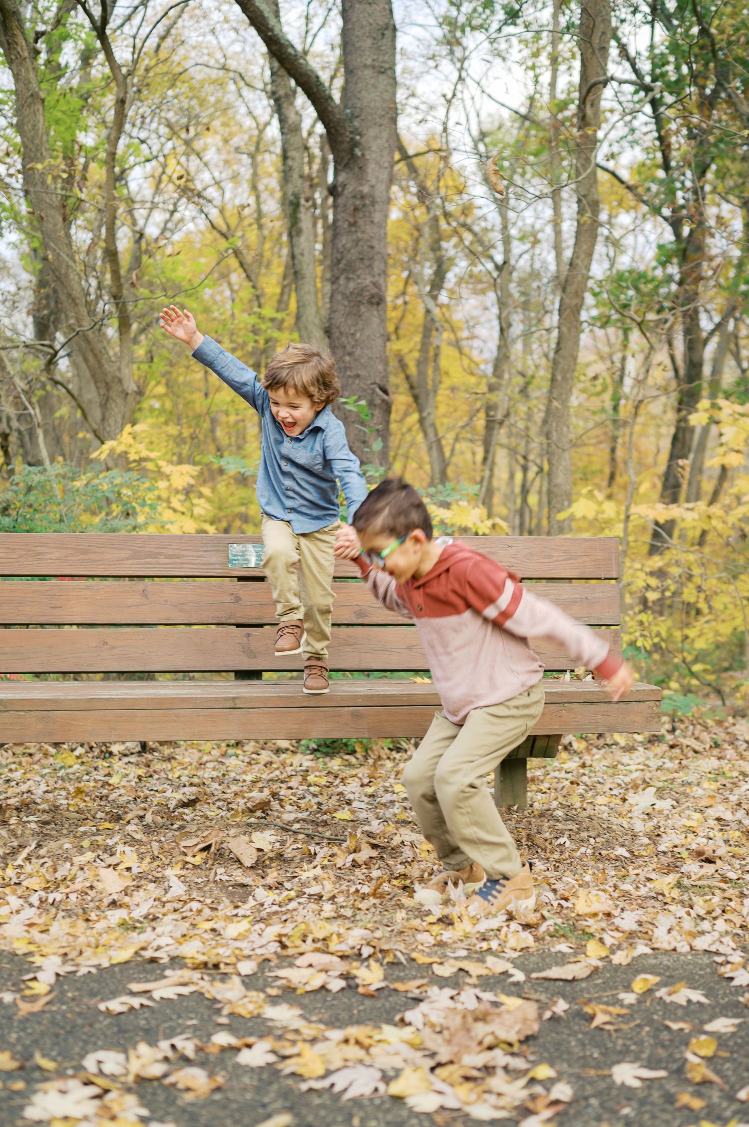 Two children playing energetically on wooden benches in autumn park.