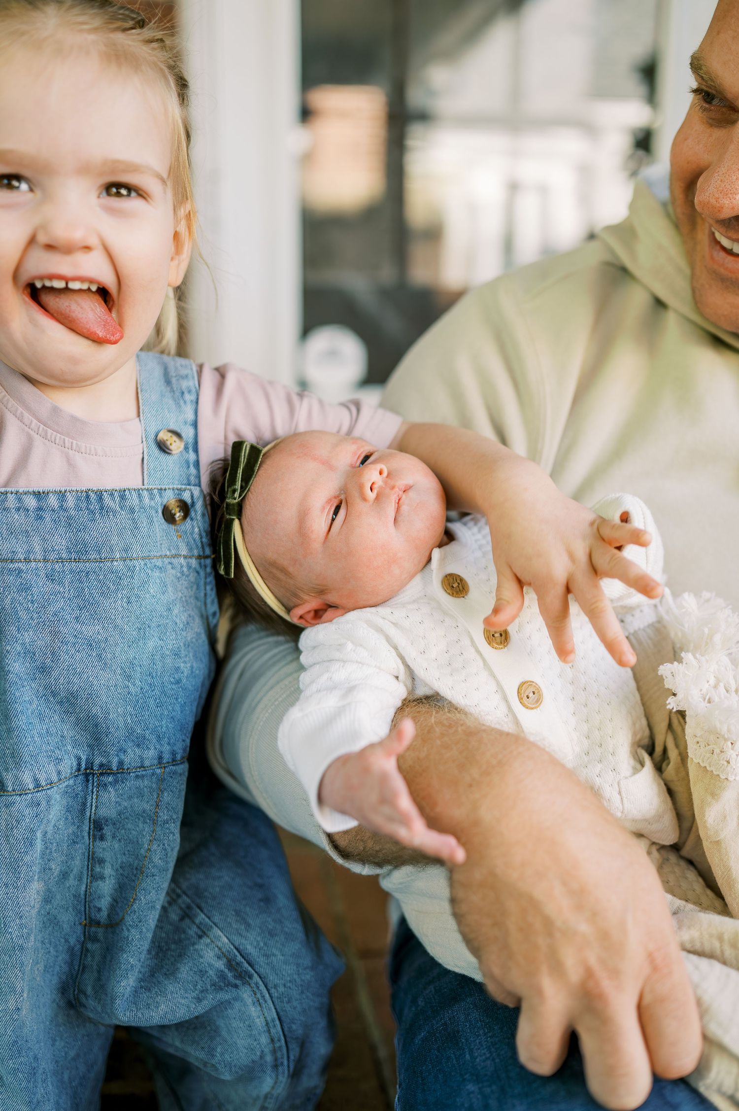 Candid family portraits showing sweet interactions with a newborn baby on a porch.