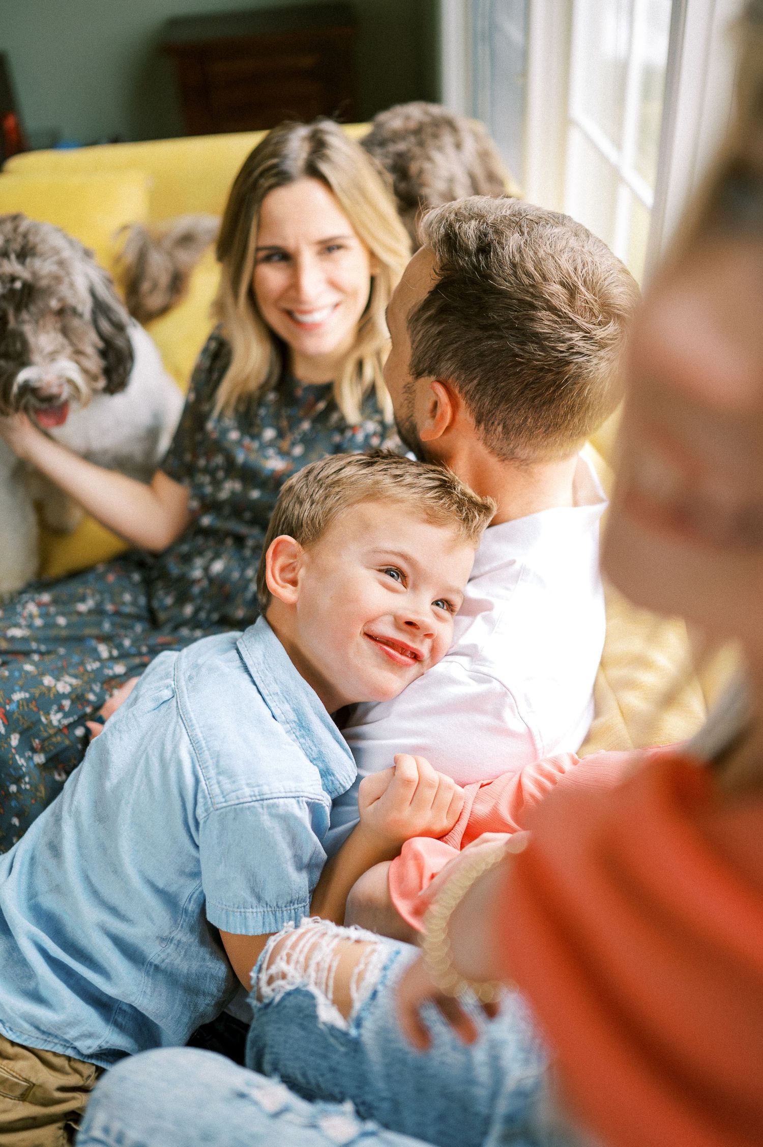 Candid moments of playful interaction on a comfortable yellow couch in a sunlit living room.