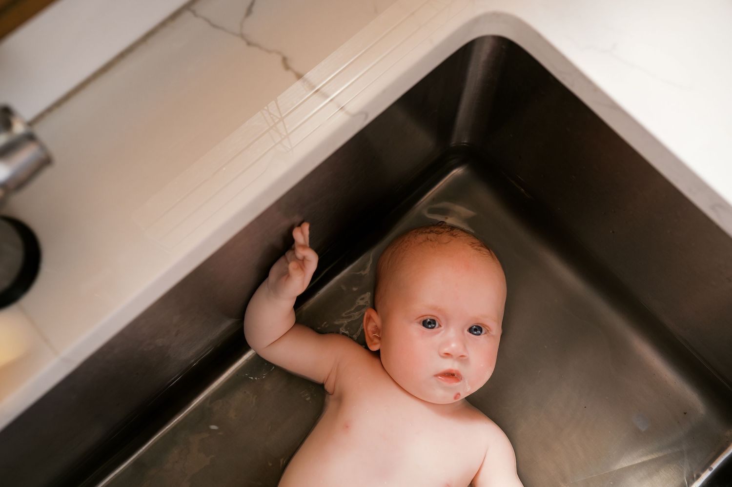 Baby looking upward while being bathed in kitchen sink.