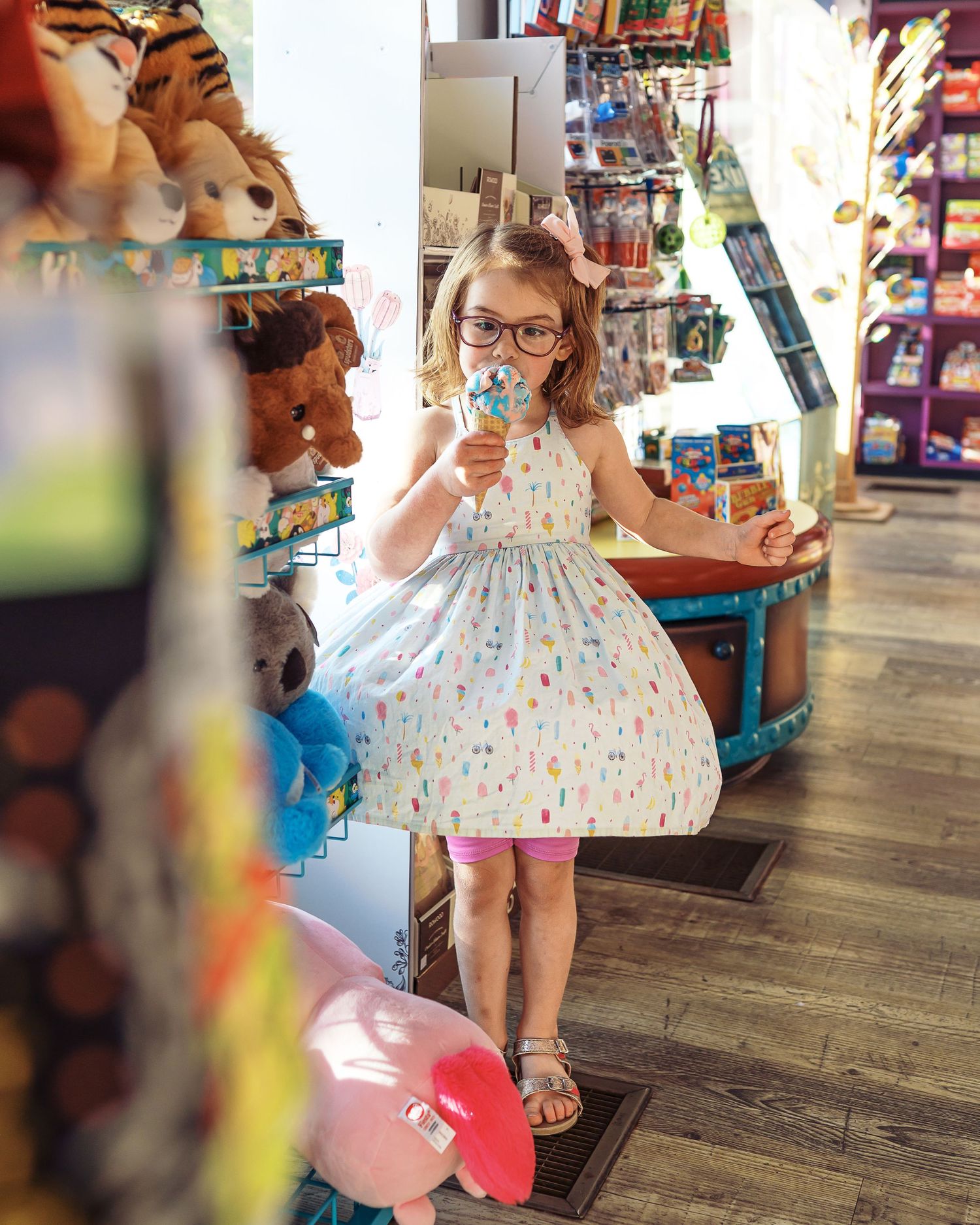Child in a polka dot dress enjoying ice cream while shopping in a candy store.