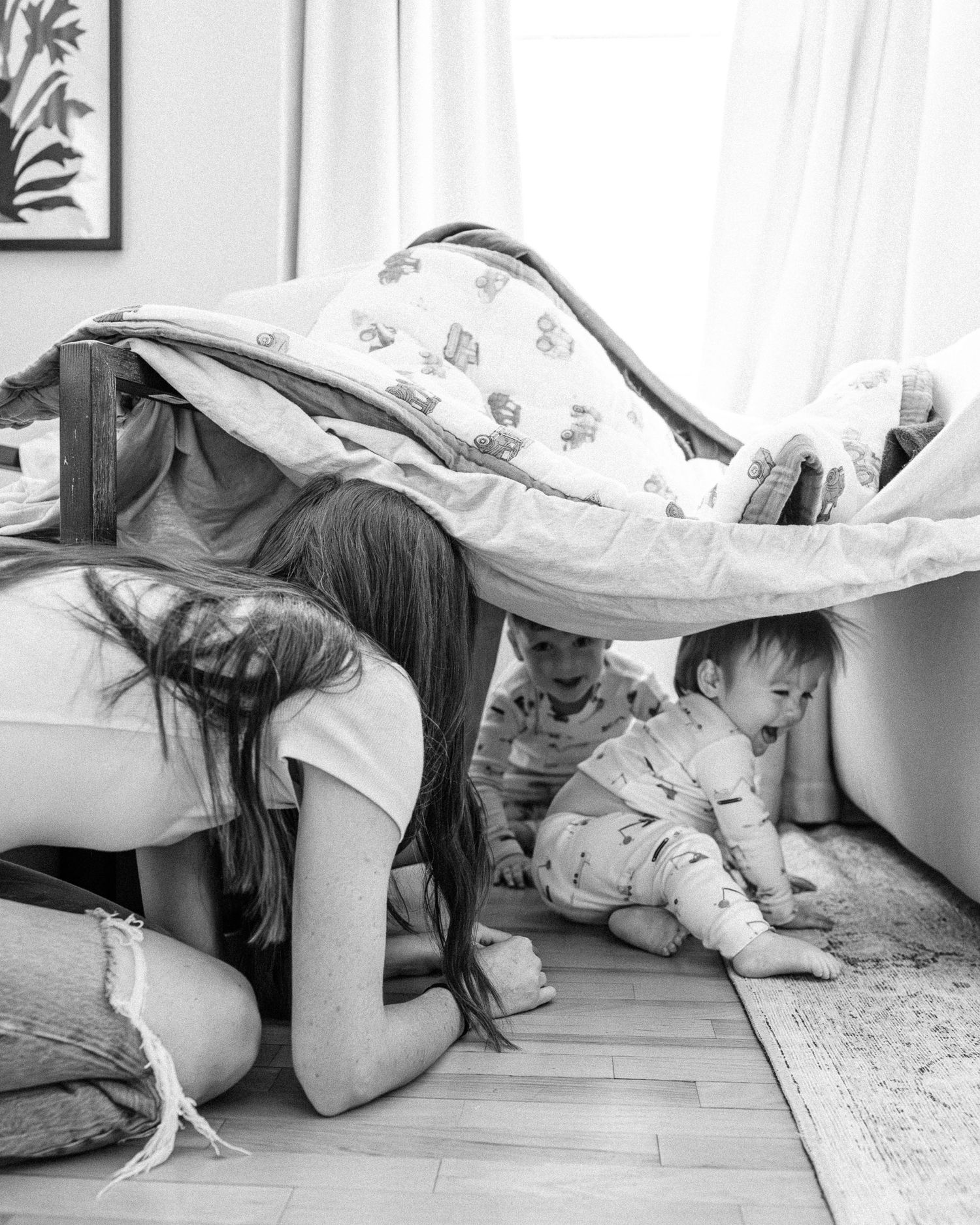 Playful moments under a blanket fort reveal joy and laughter on hardwood floors.