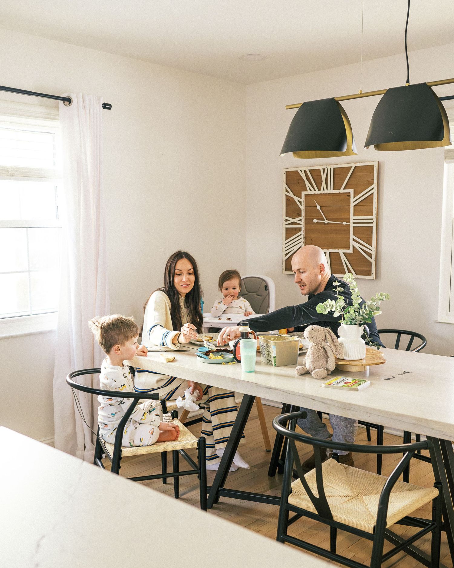 A bright modern dining room with black chairs and white walls features a decorative sunburst clock.