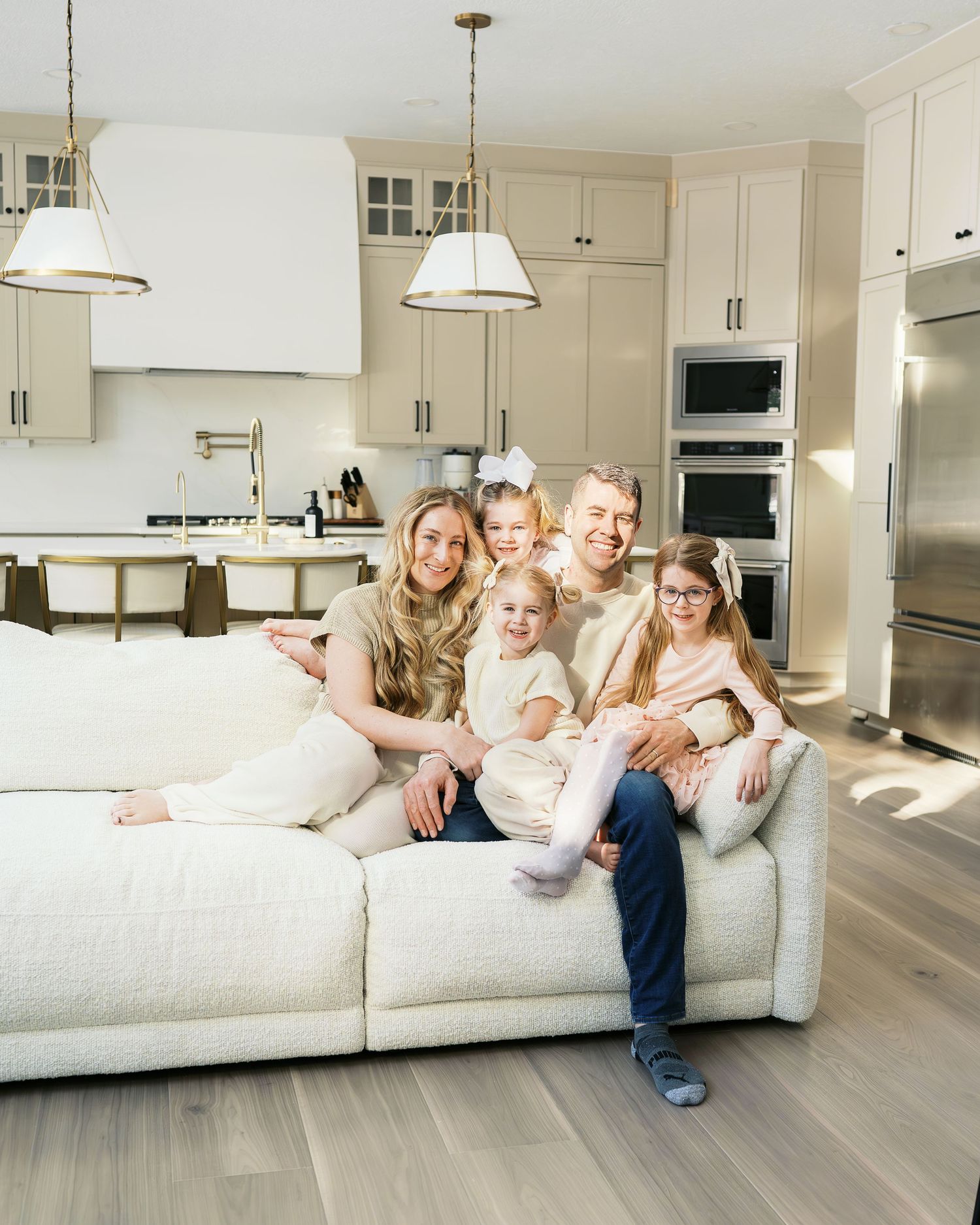 A family relaxes together on a white sectional sofa in a bright, modern kitchen space.