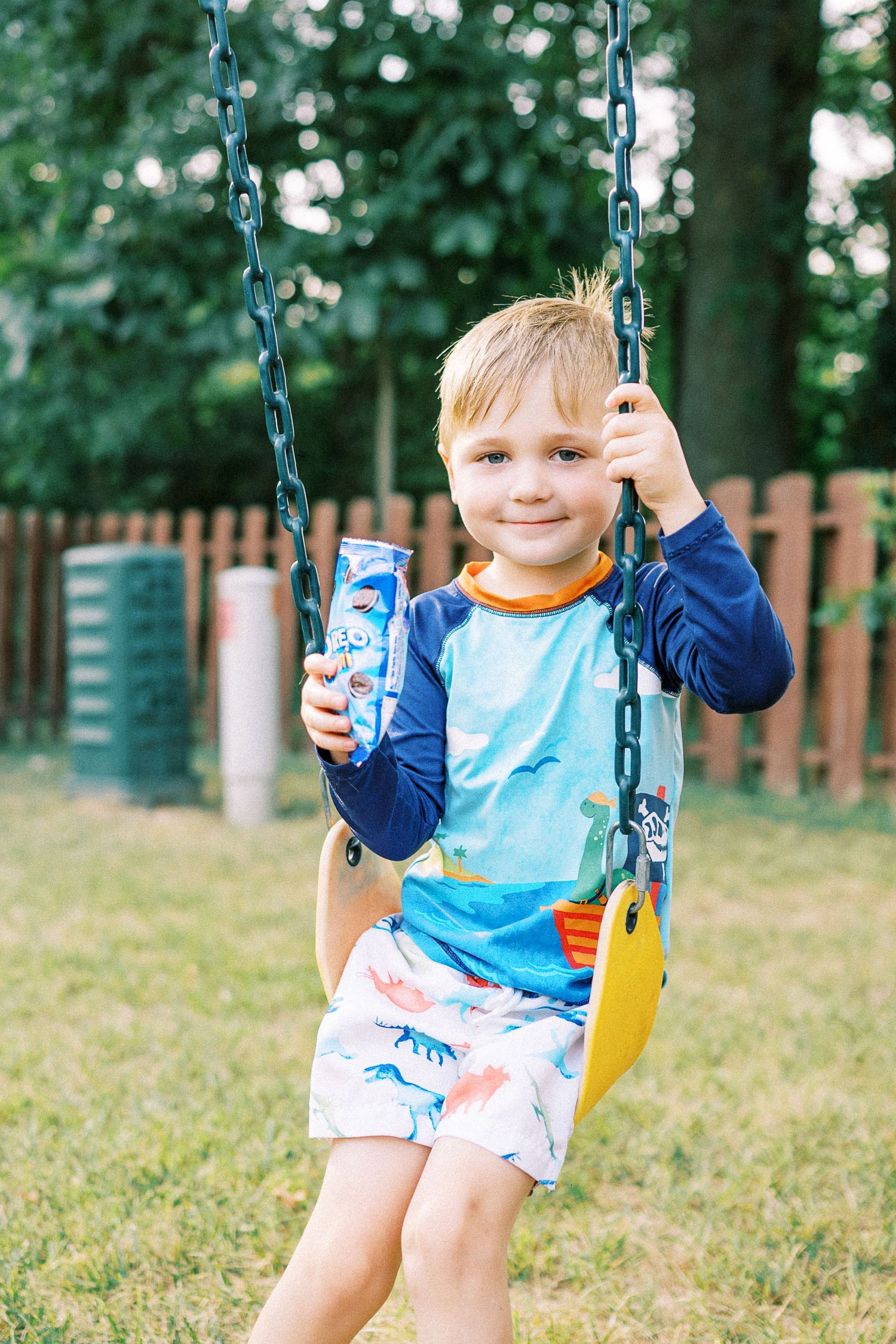 Child swinging on blue chain swing in backyard garden.