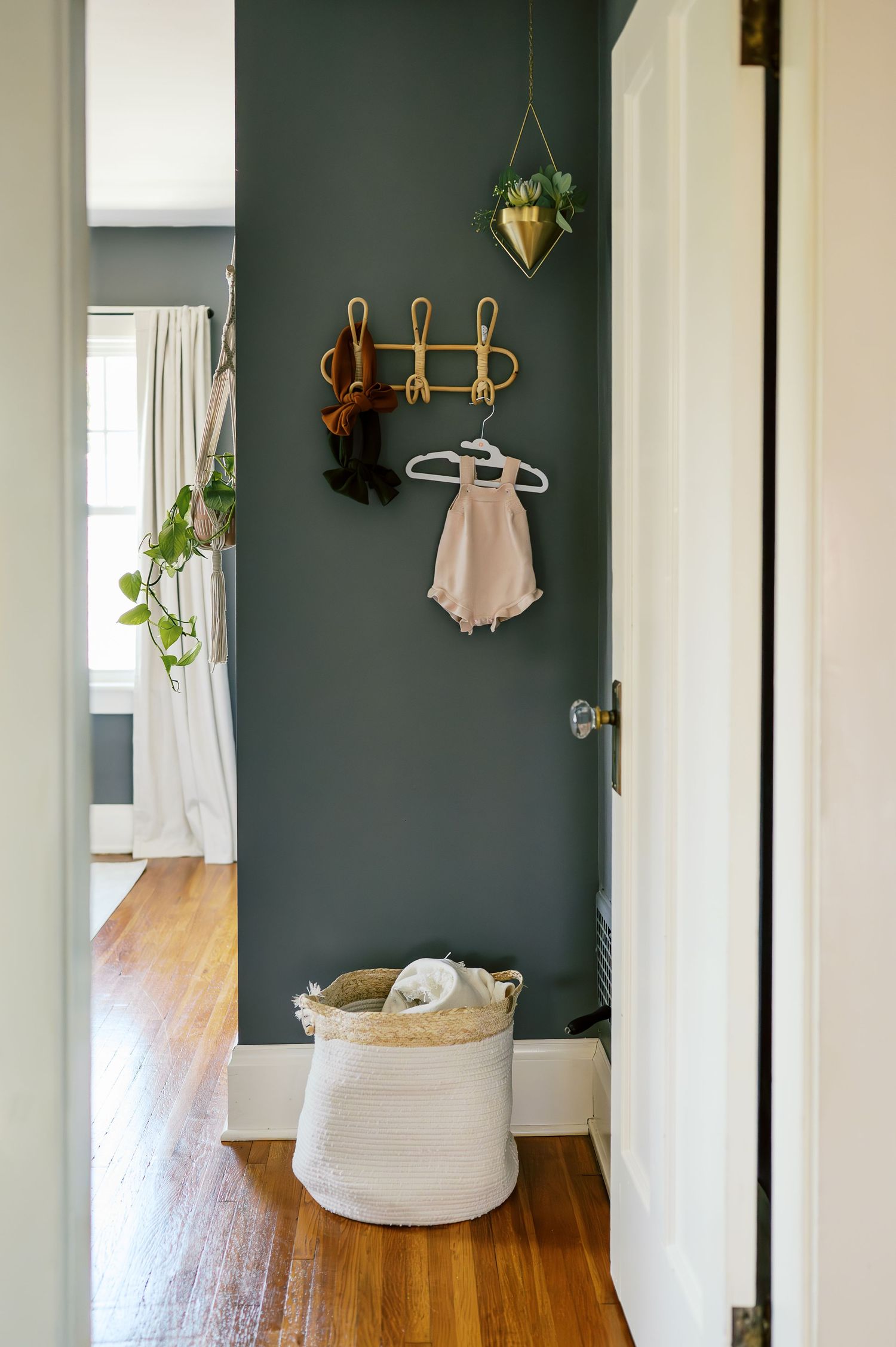 A minimalist hallway with sage green walls, wooden hooks, and a storage basket on hardwood floors.
