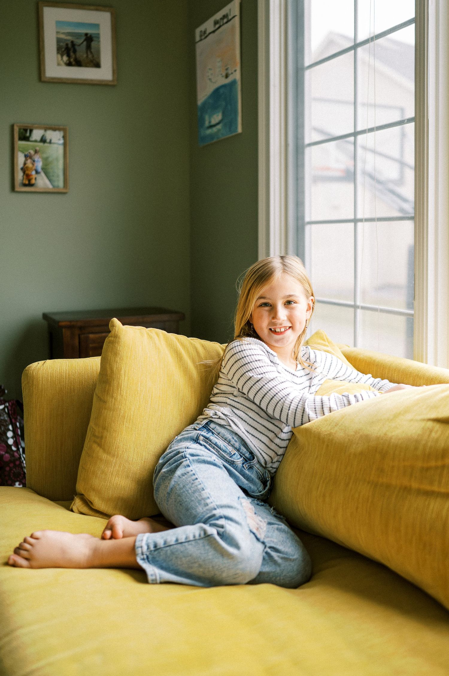 Someone relaxes on a yellow sofa in a room with green walls and window light.