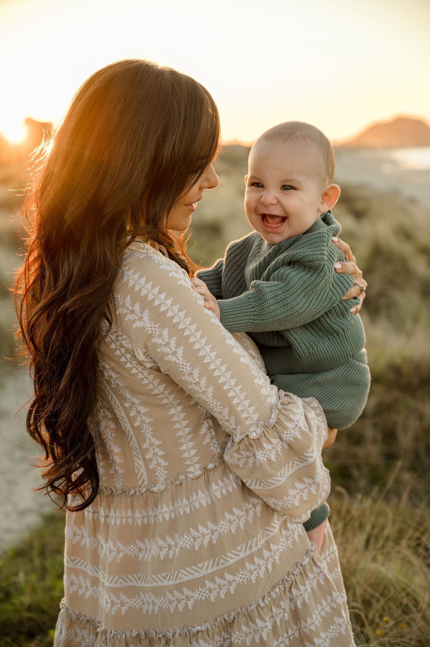 A tender moment between parent and baby during golden hour, wearing a patterned sweater in a natural outdoor setting.