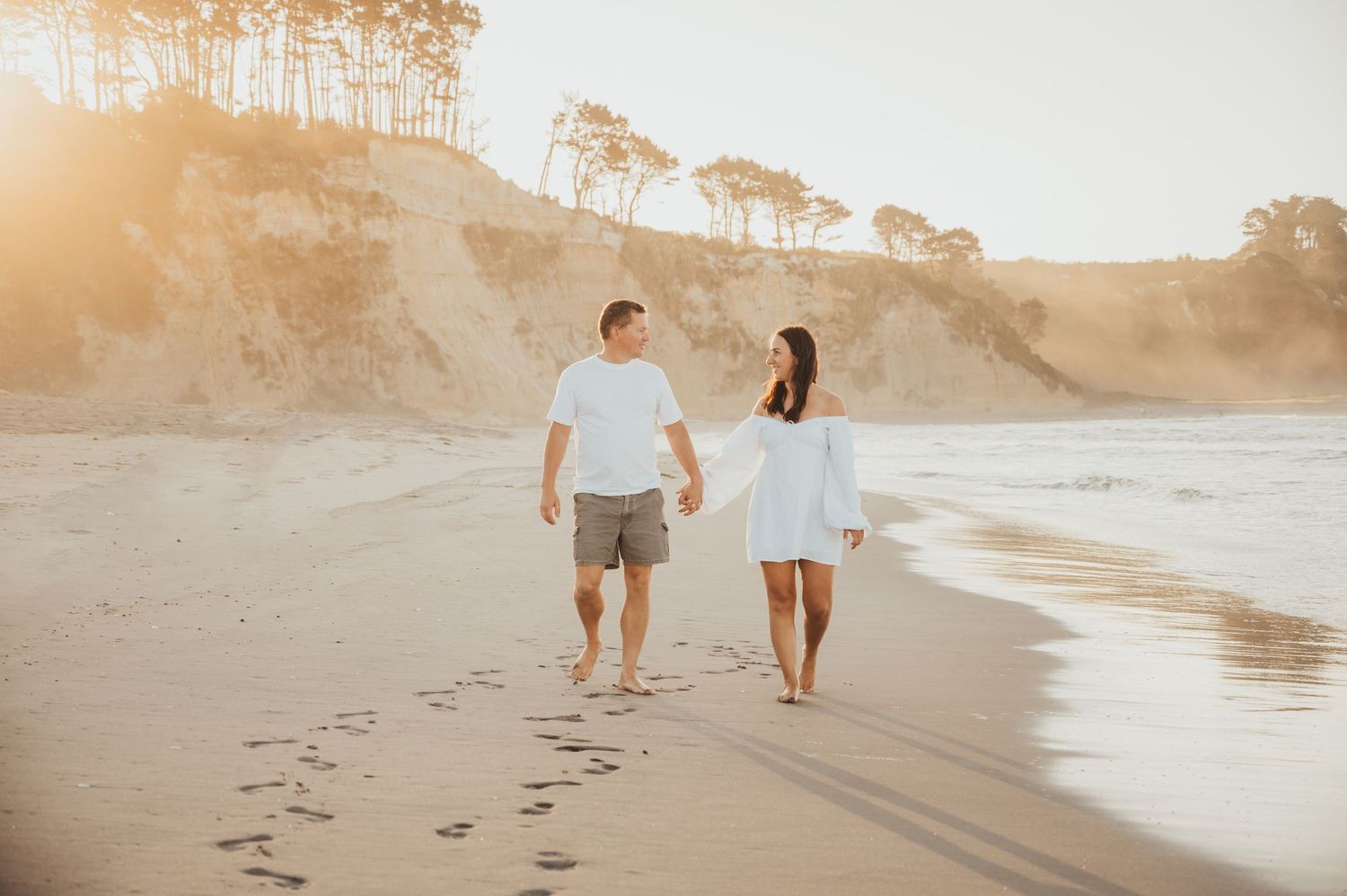 Romantic couple walking on beach at sunset leaving footprints in sand.