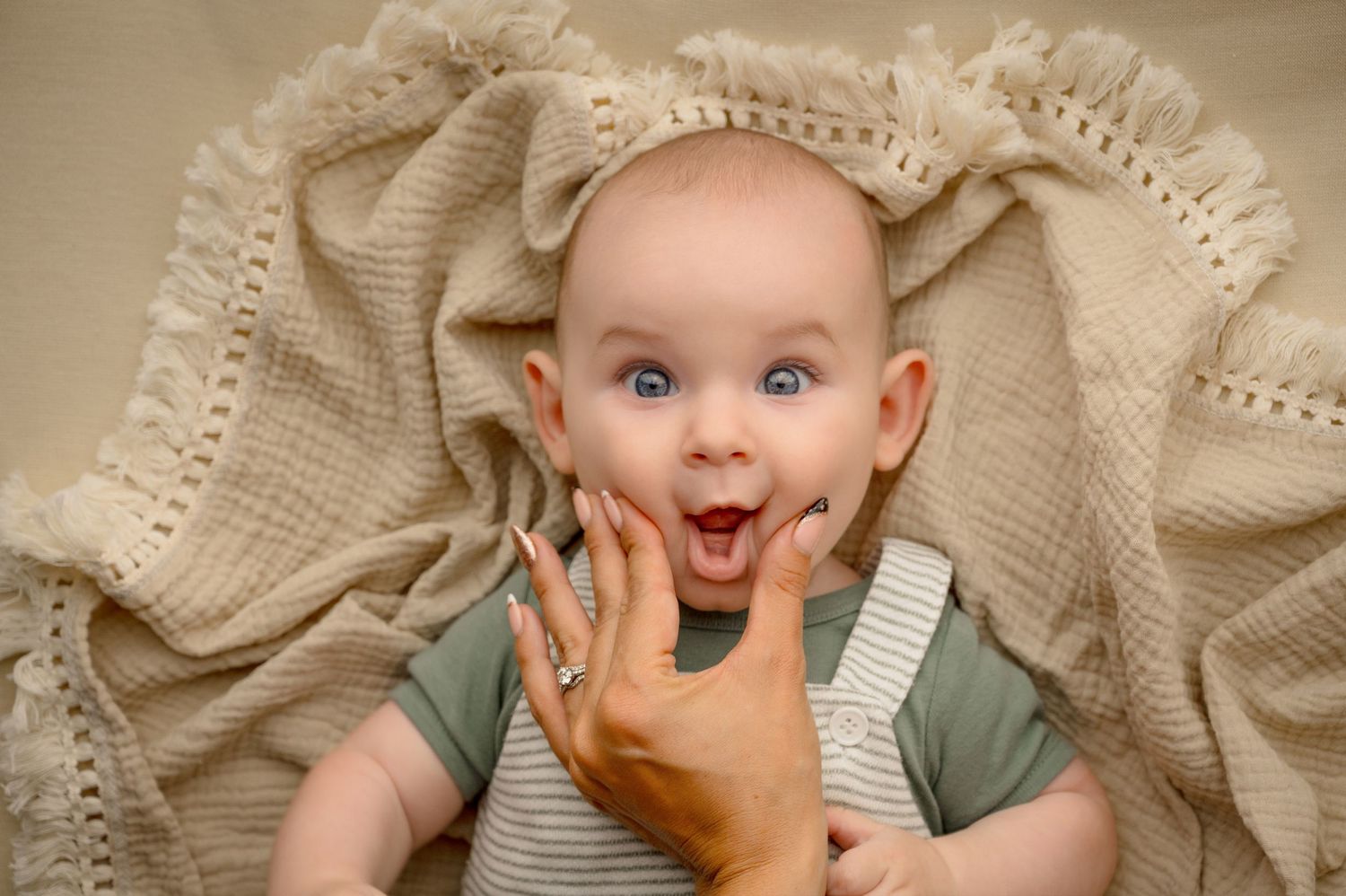 Joyful baby portrait on cream knit blanket with expressive smile.