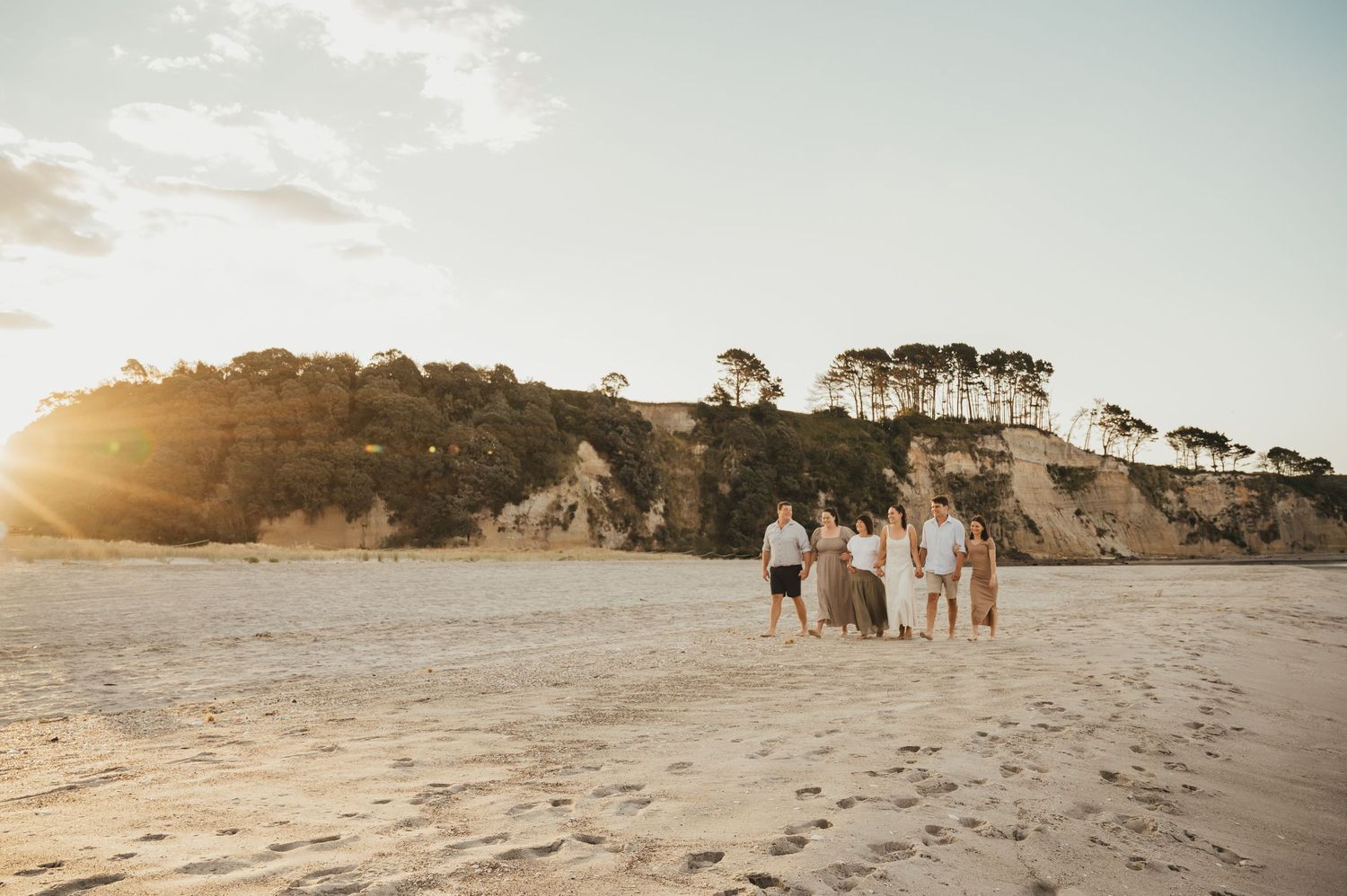 Group walks along scenic coastal beach at sunset with golden light illuminating the rugged cliffs and shoreline.