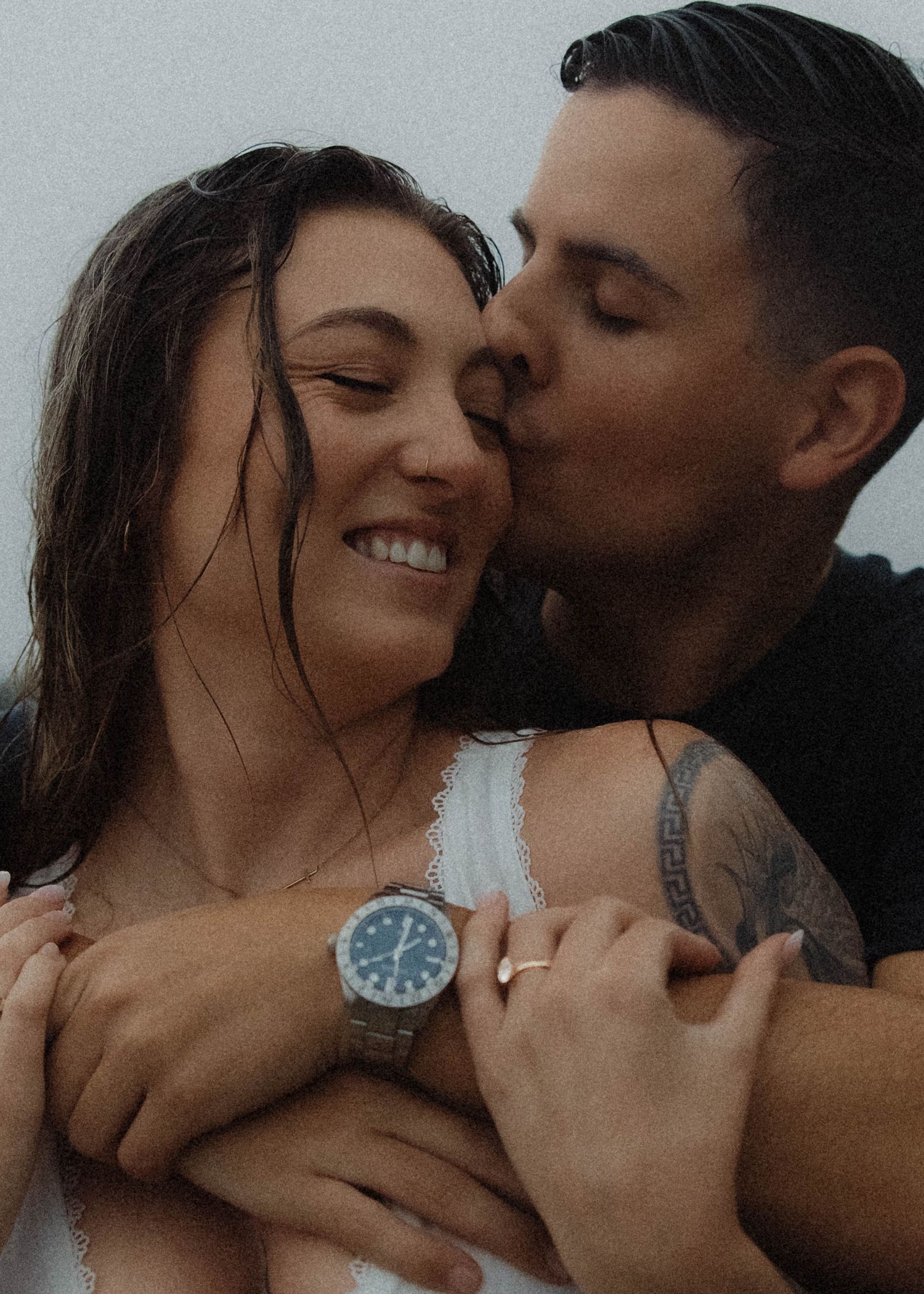 Man with tattoos kisses smiling woman on the cheek during a romantic couples portrait session.