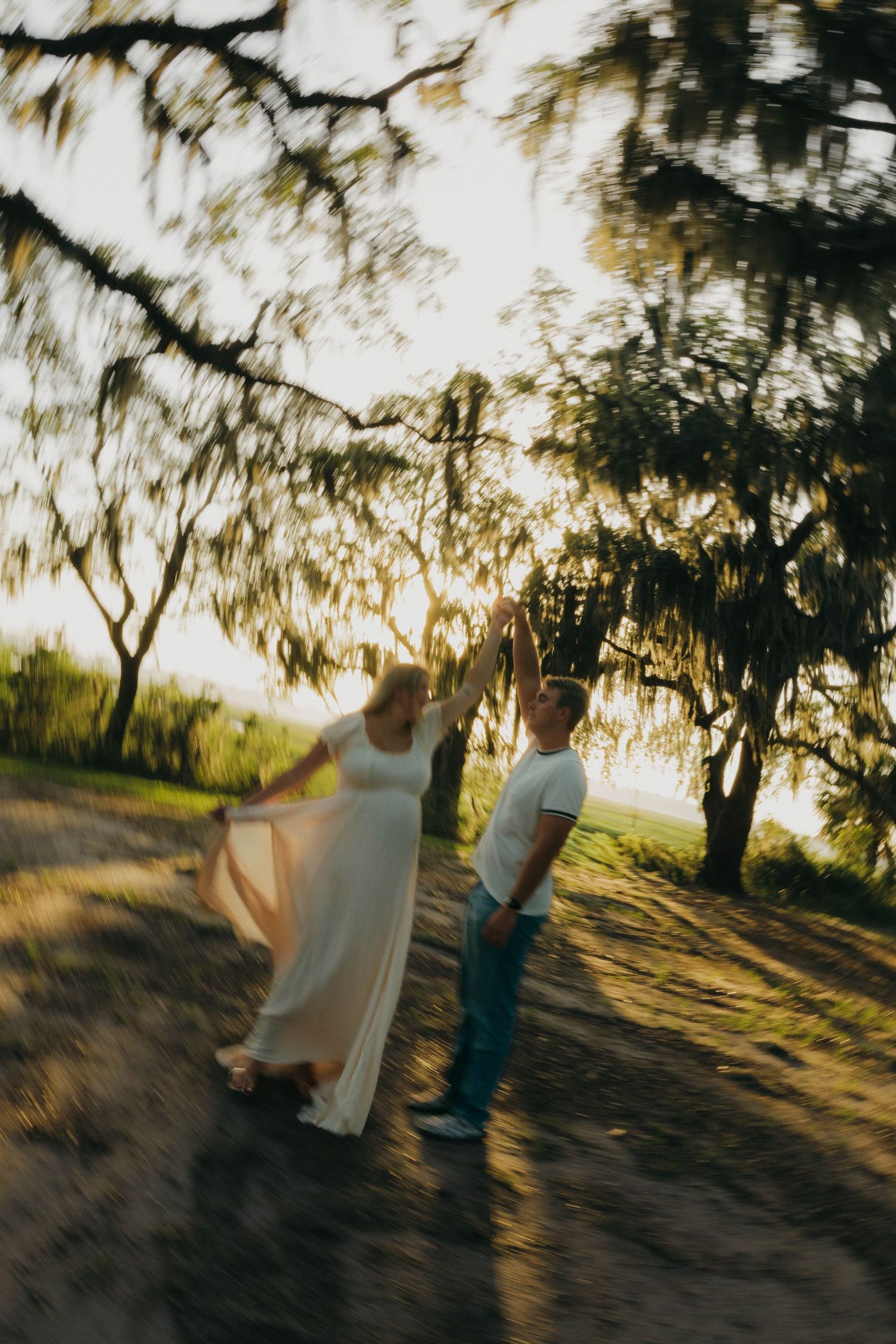 Couple dances under Spanish moss-draped trees in golden sunset light, woman in flowing white dress.