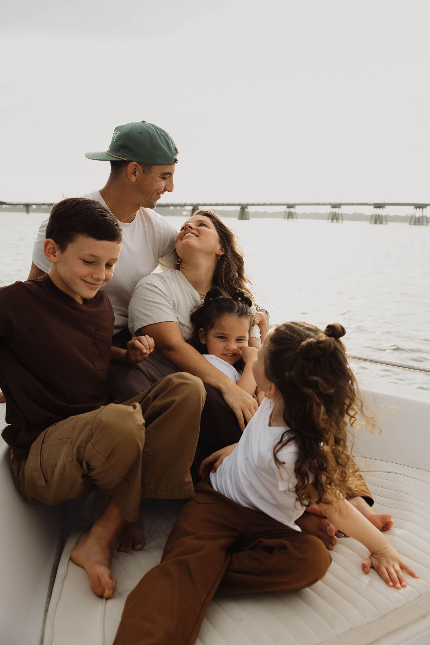 Happy family of five relaxes together on a boat deck near a waterway, laughing and cuddling.
