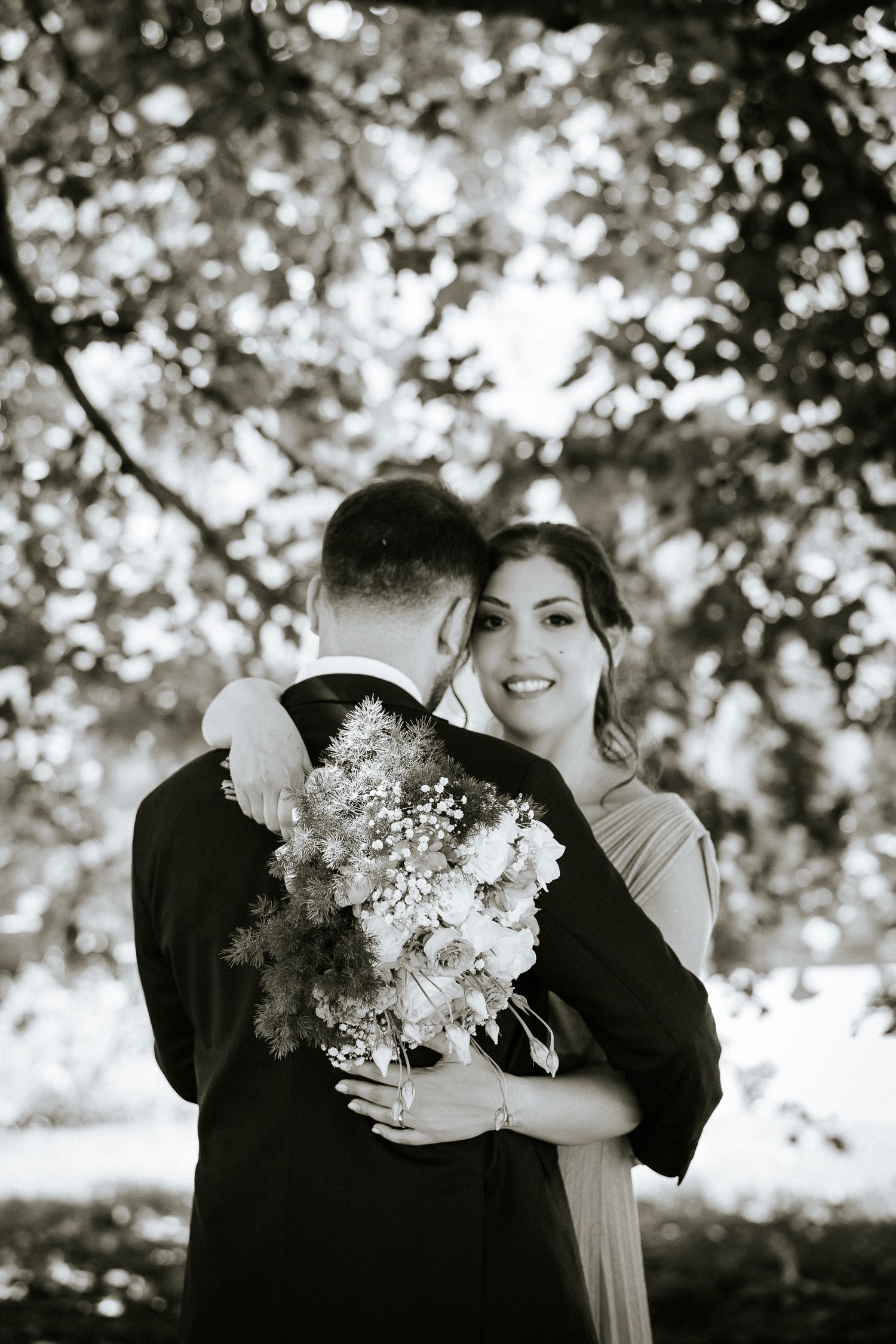 A romantic black and white photo series showing a couple embracing while holding delicate white floral bouquets outdoors.