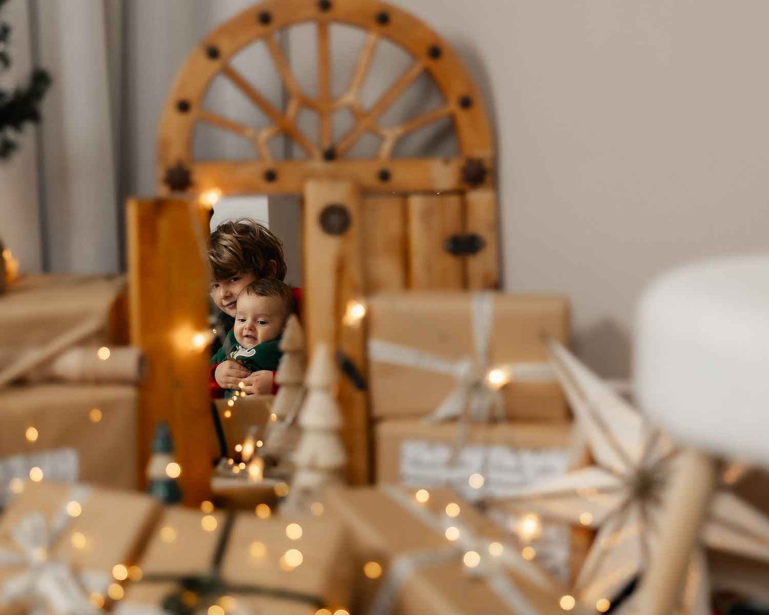A mother and child are reflected in a mirror surrounded by wrapped Christmas gifts and twinkling fairy lights.