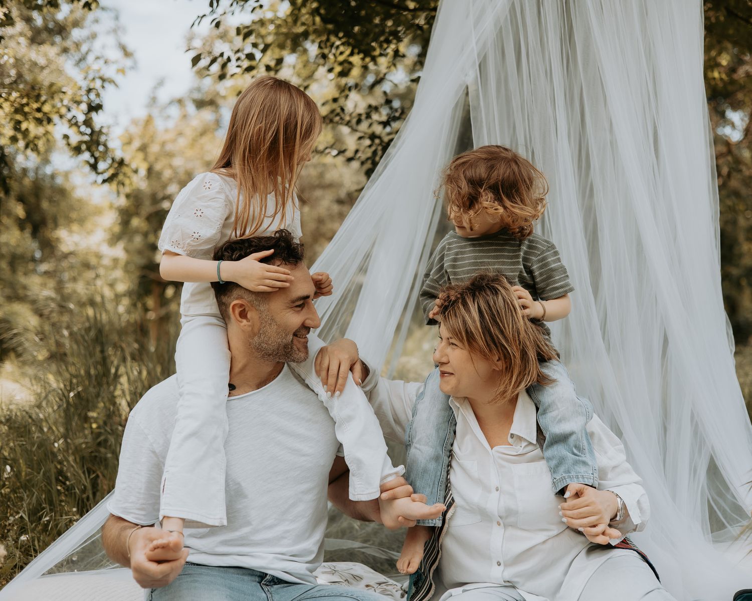 Casual family photo session with white fabric backdrop in nature setting.