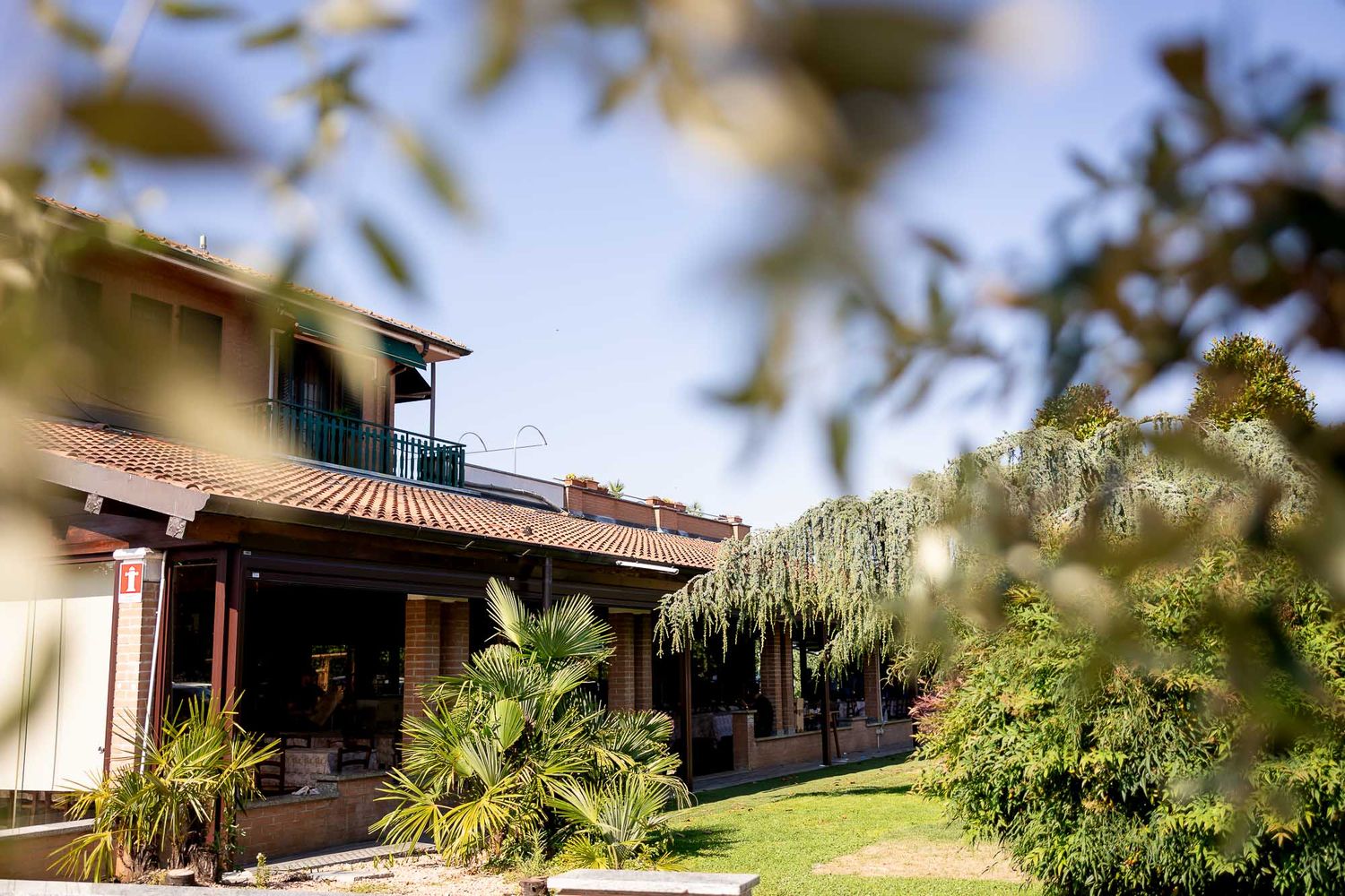 Charming Italian countryside villa with terracotta roof surrounded by lush green trees and garden.