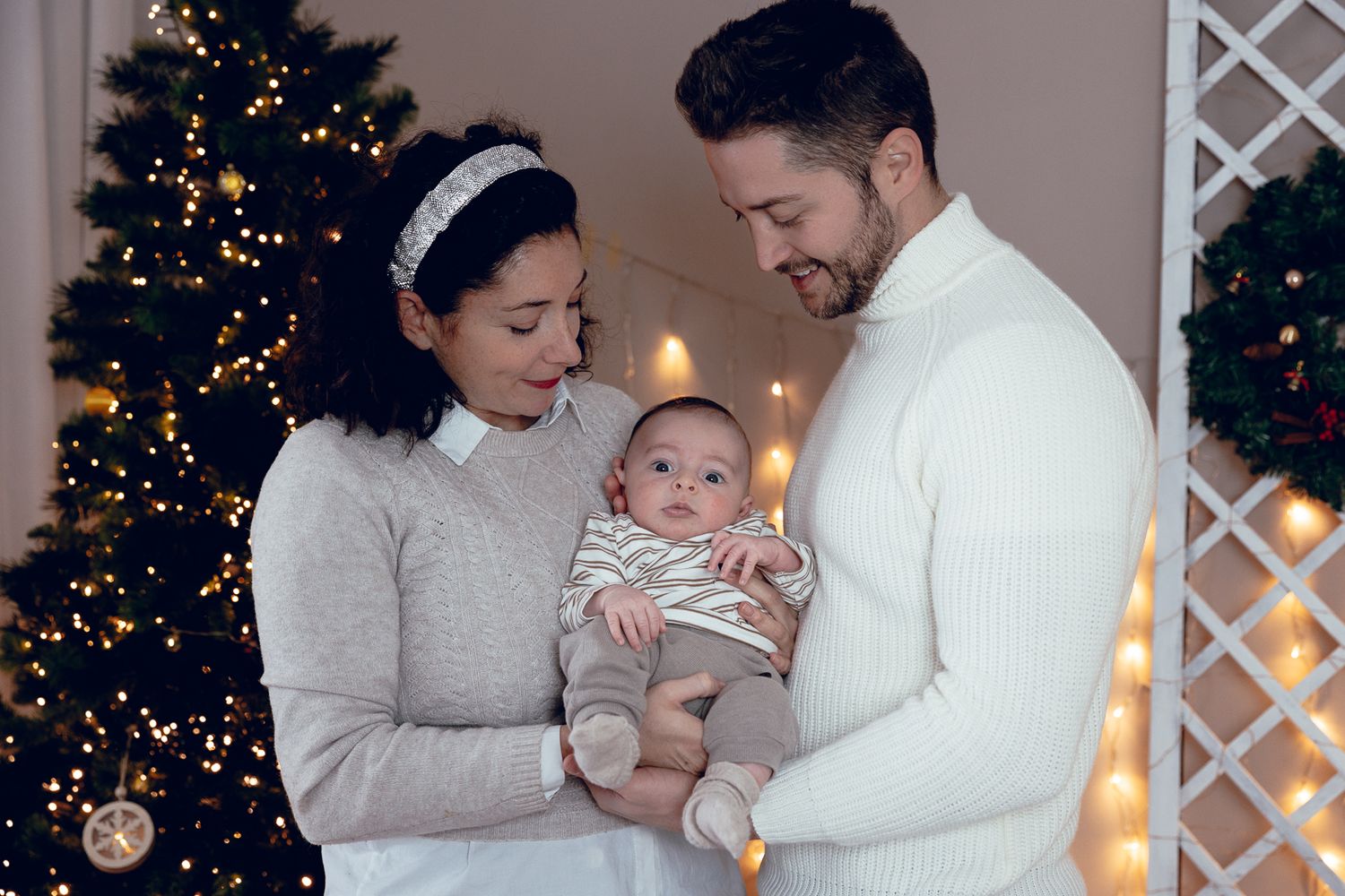 A family poses together in front of a Christmas tree with twinkling lights in a cozy holiday setting.