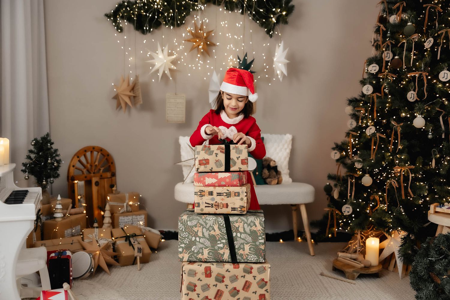 A young girl in a Santa hat opens Christmas gifts surrounded by festive decorations and a decorated tree.