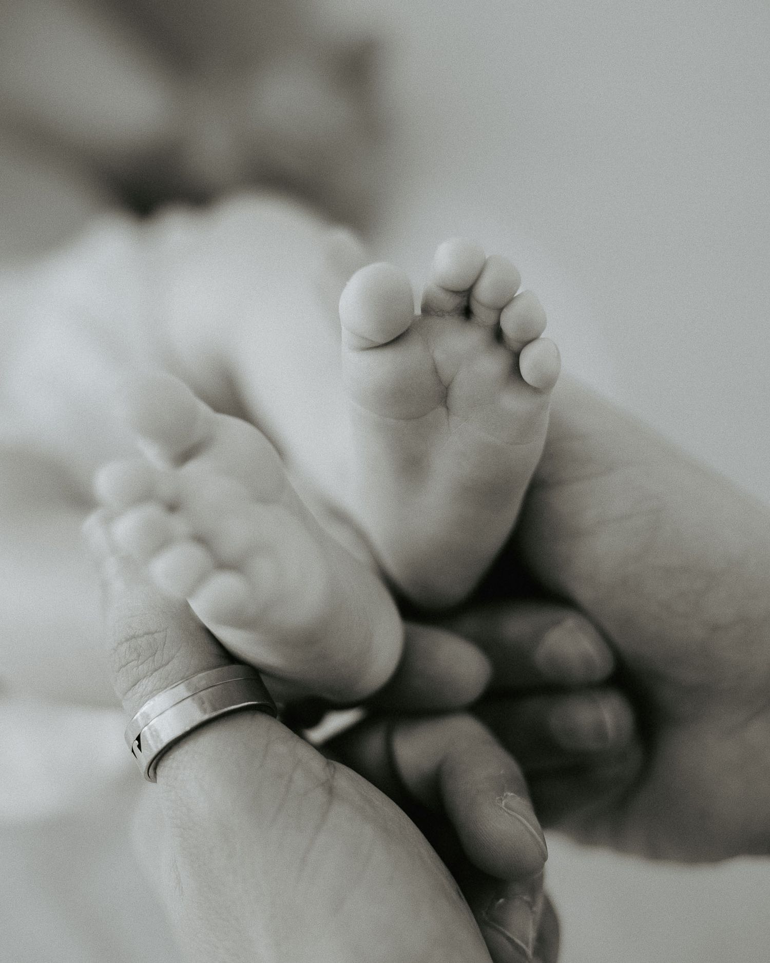 Dettaglio dei piedini del neonato tra le mani dei genitori.