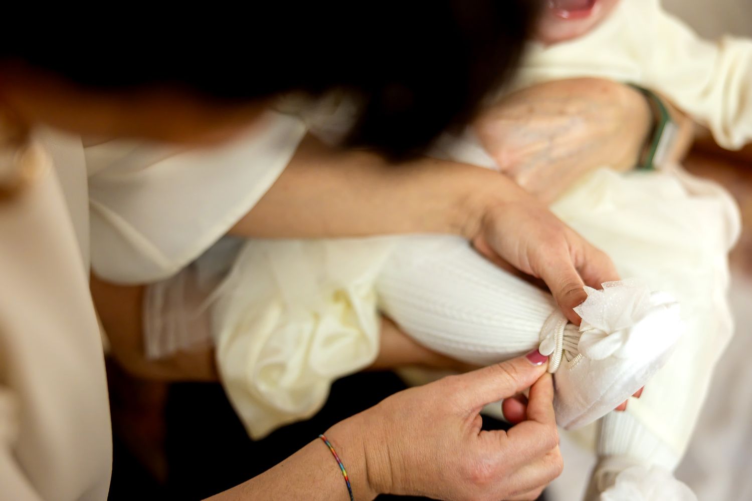 Woman dressing a newborn baby in a white christening gown with delicate details.