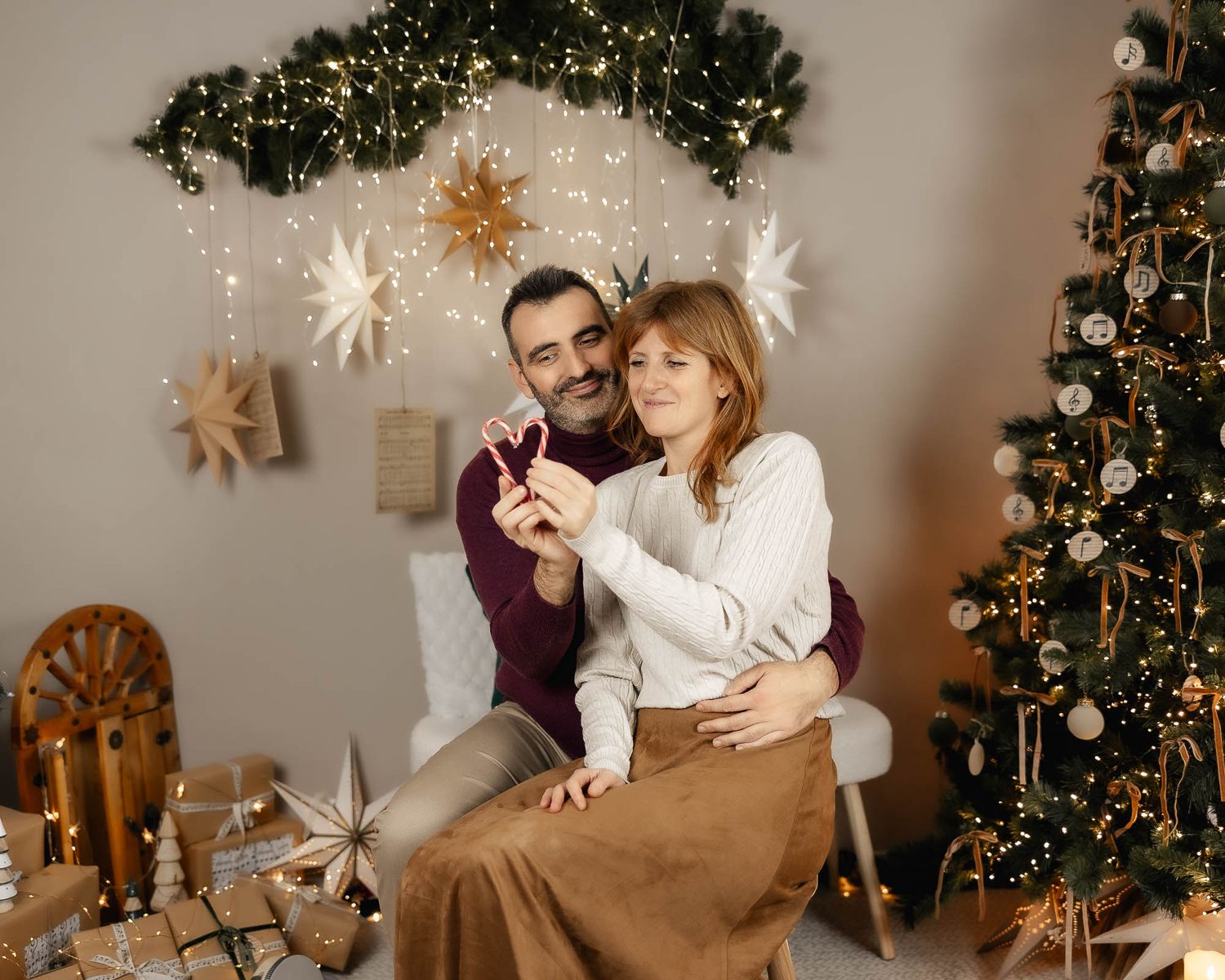 A couple celebrates Christmas holding sparklers near a decorated tree with gifts and festive star ornaments.