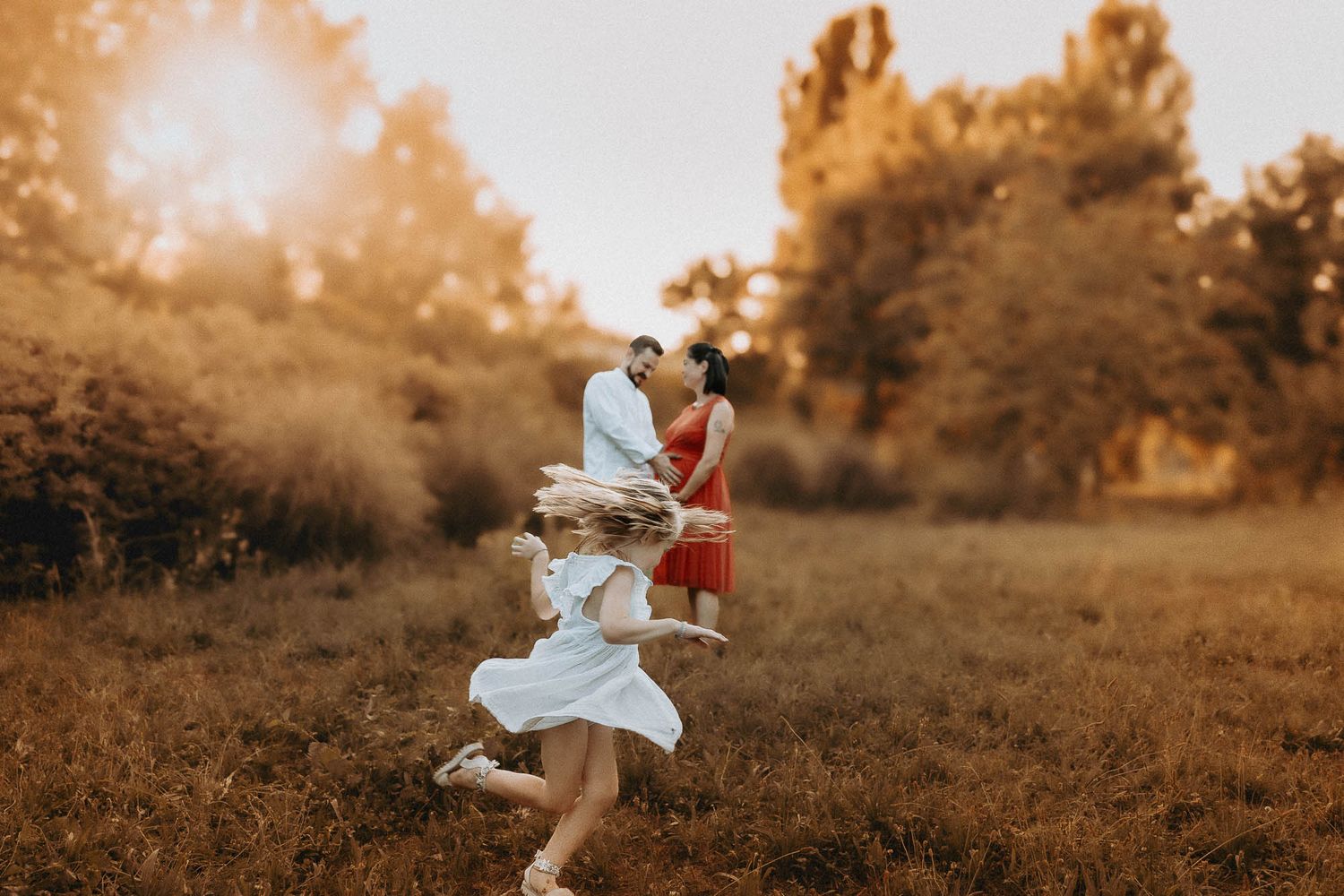 Un gioioso momento di famiglia al tramonto, con un bambino che corre verso i genitori mentre si baciano in un prato al tramonto