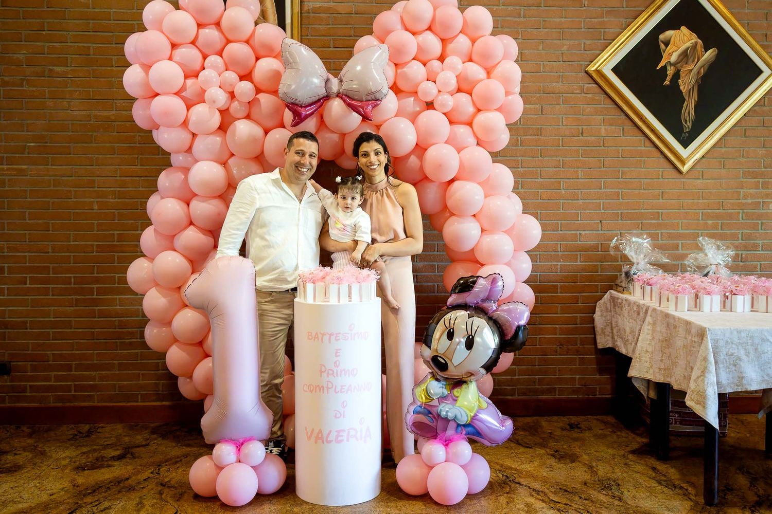 Family posing at a pink Minnie Mouse first birthday party with balloon arch and cake.