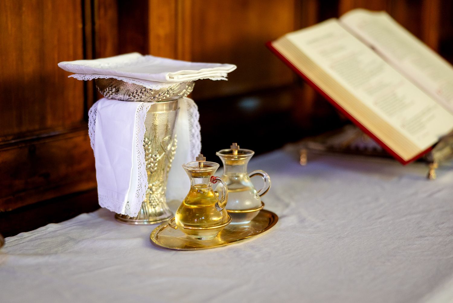 Gold chalice and cruets on altar with open Bible during Catholic Mass ceremony.