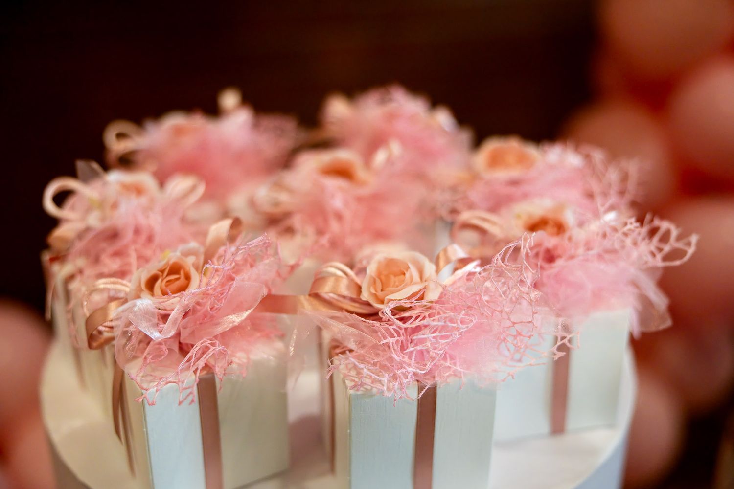 Elegant white striped gift boxes topped with pink roses and tulle decorations arranged on a tiered display.